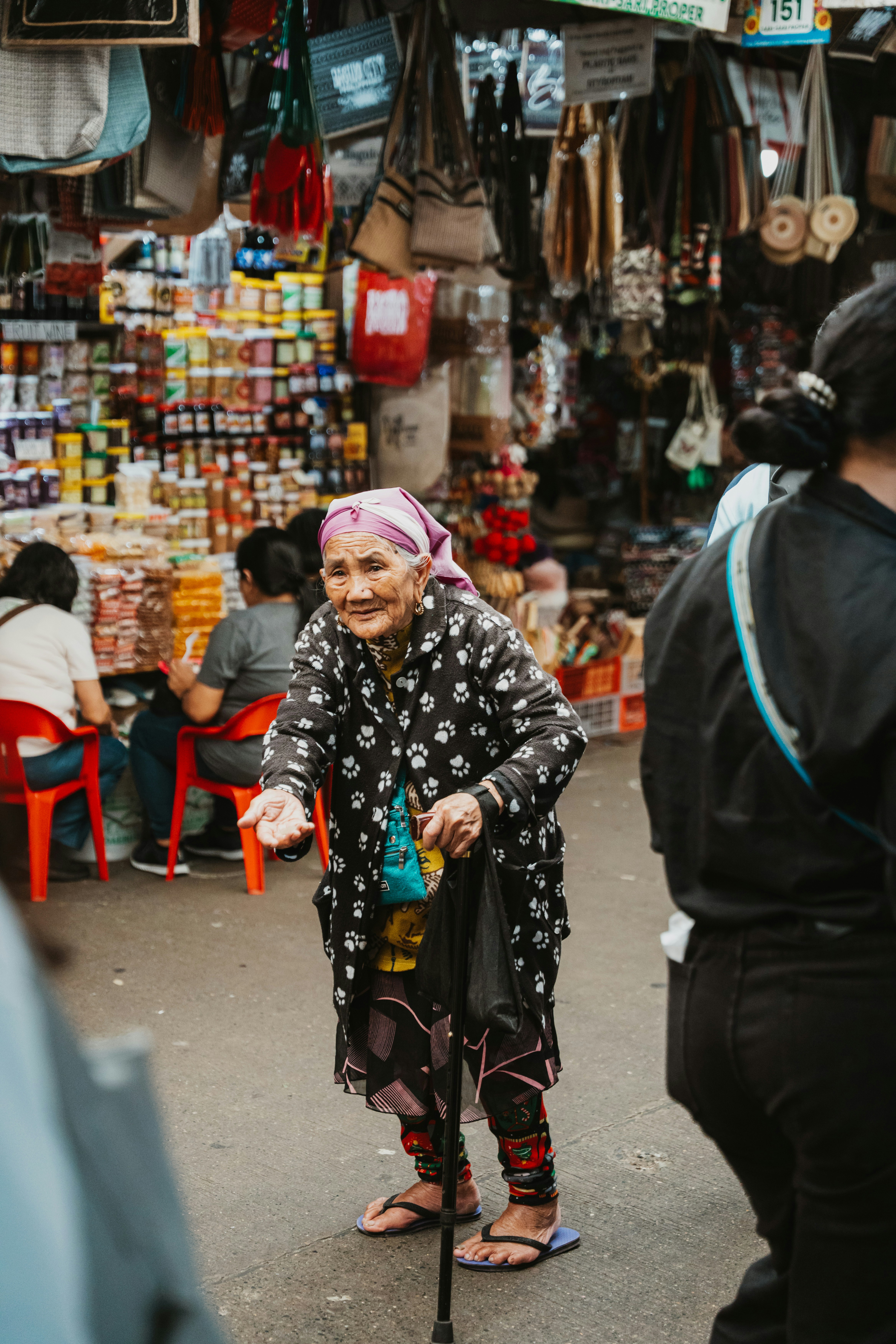 An elderly woman with a cane and headscarf in a crowded market