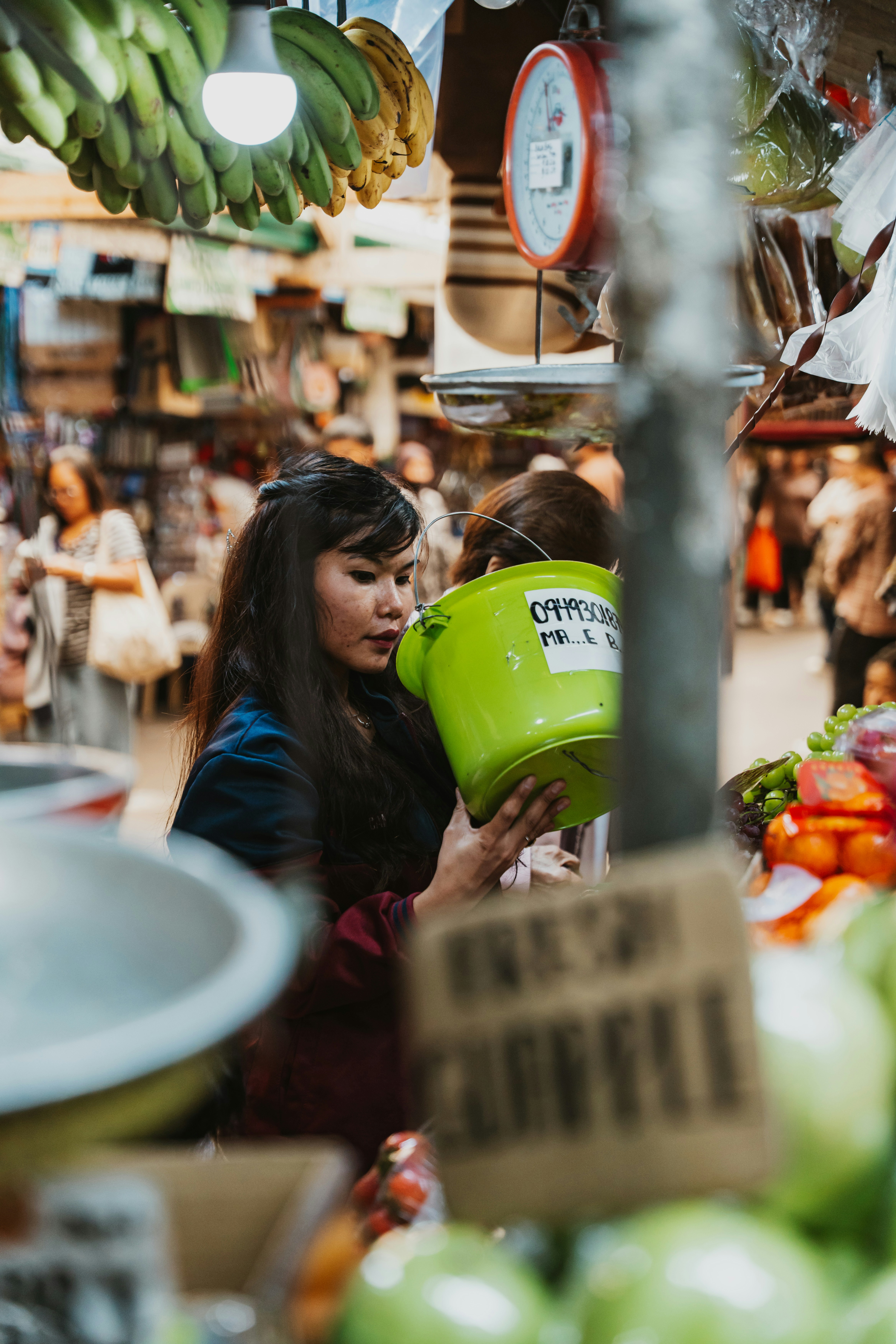 A woman holding a green plastic bucket in a busy outdoor produce market
