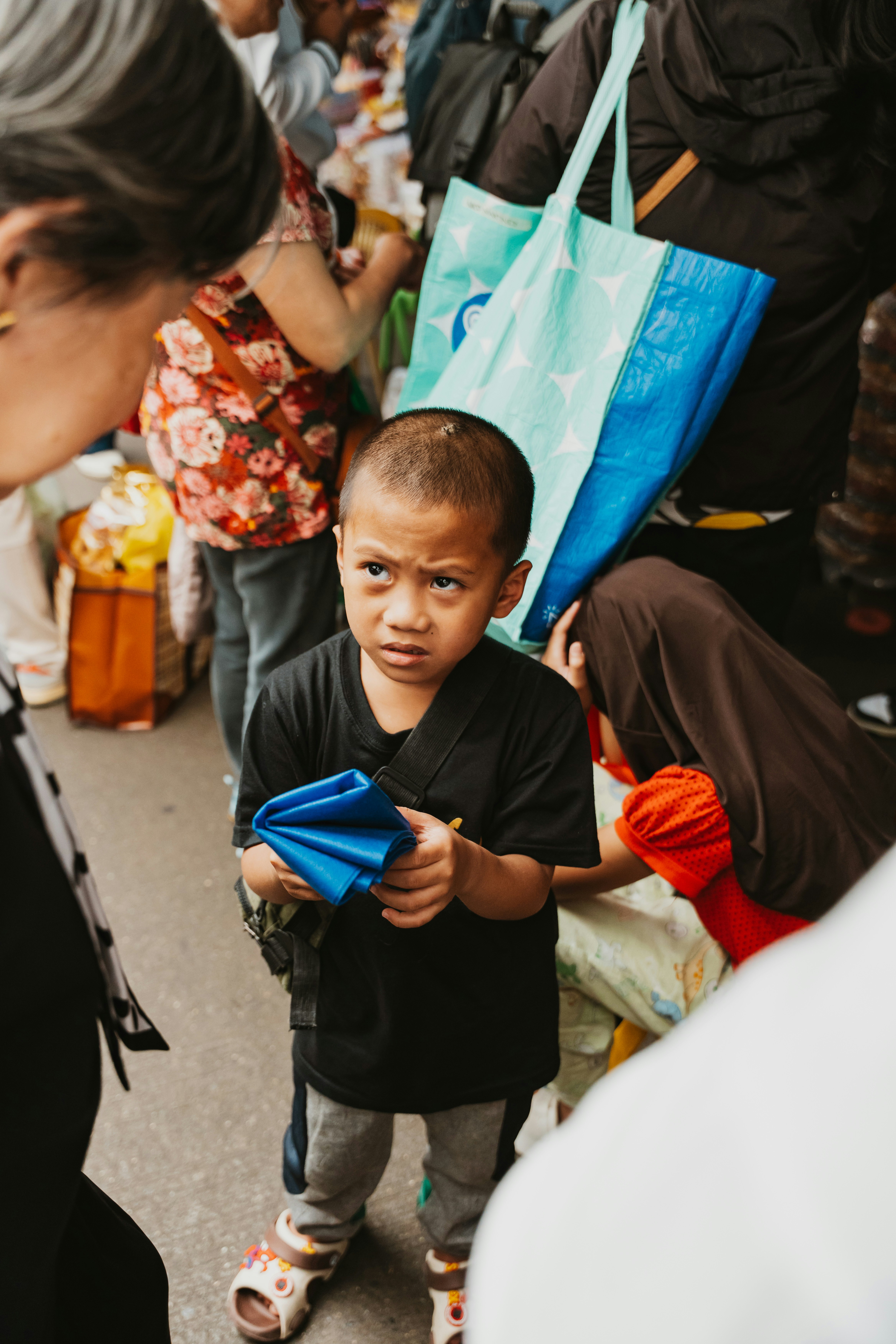 A young boy in a black t-shirt holding a blue cloth in a crowd