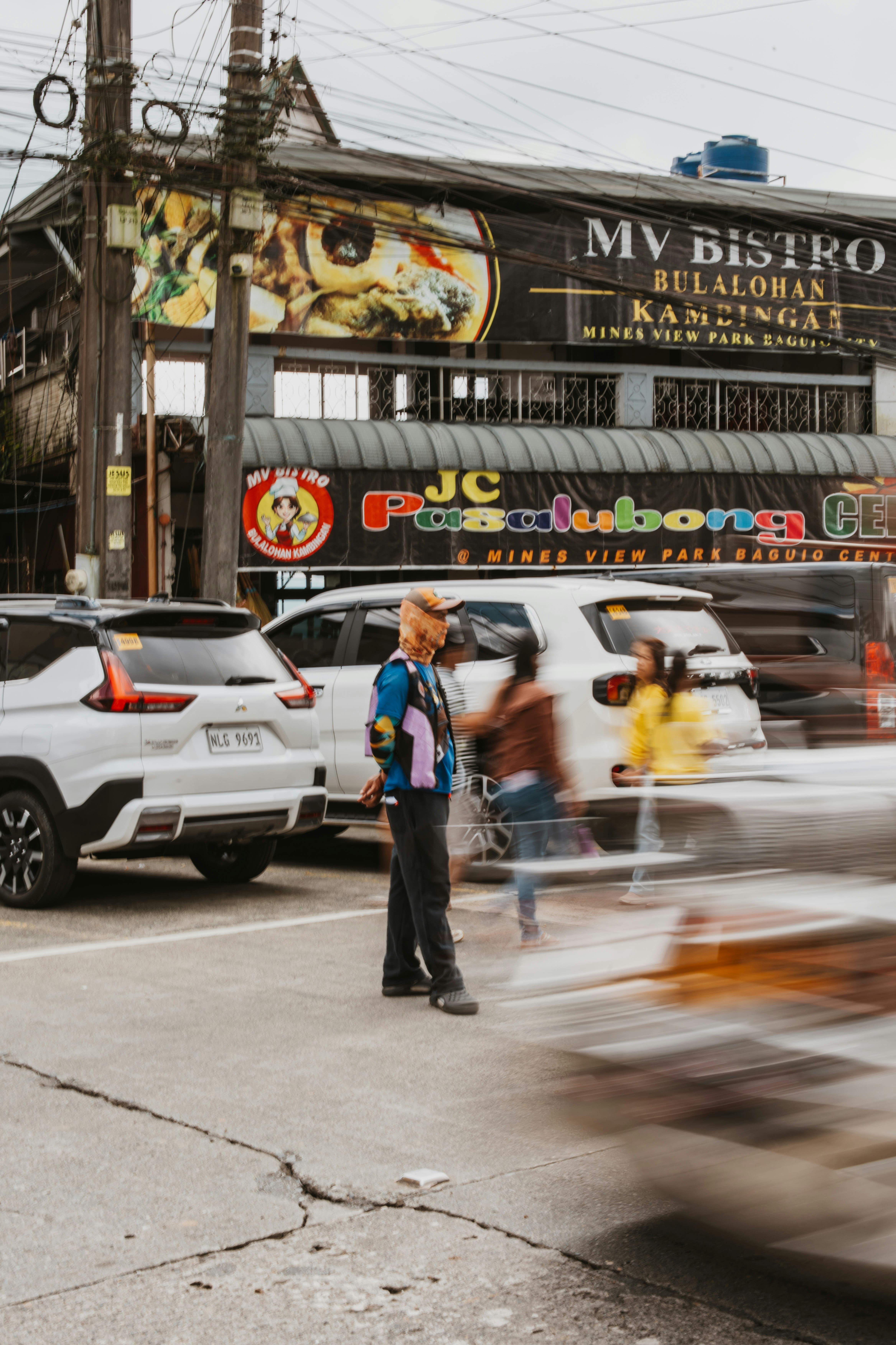 A person in a colorful vest and cap on a street in Baguio