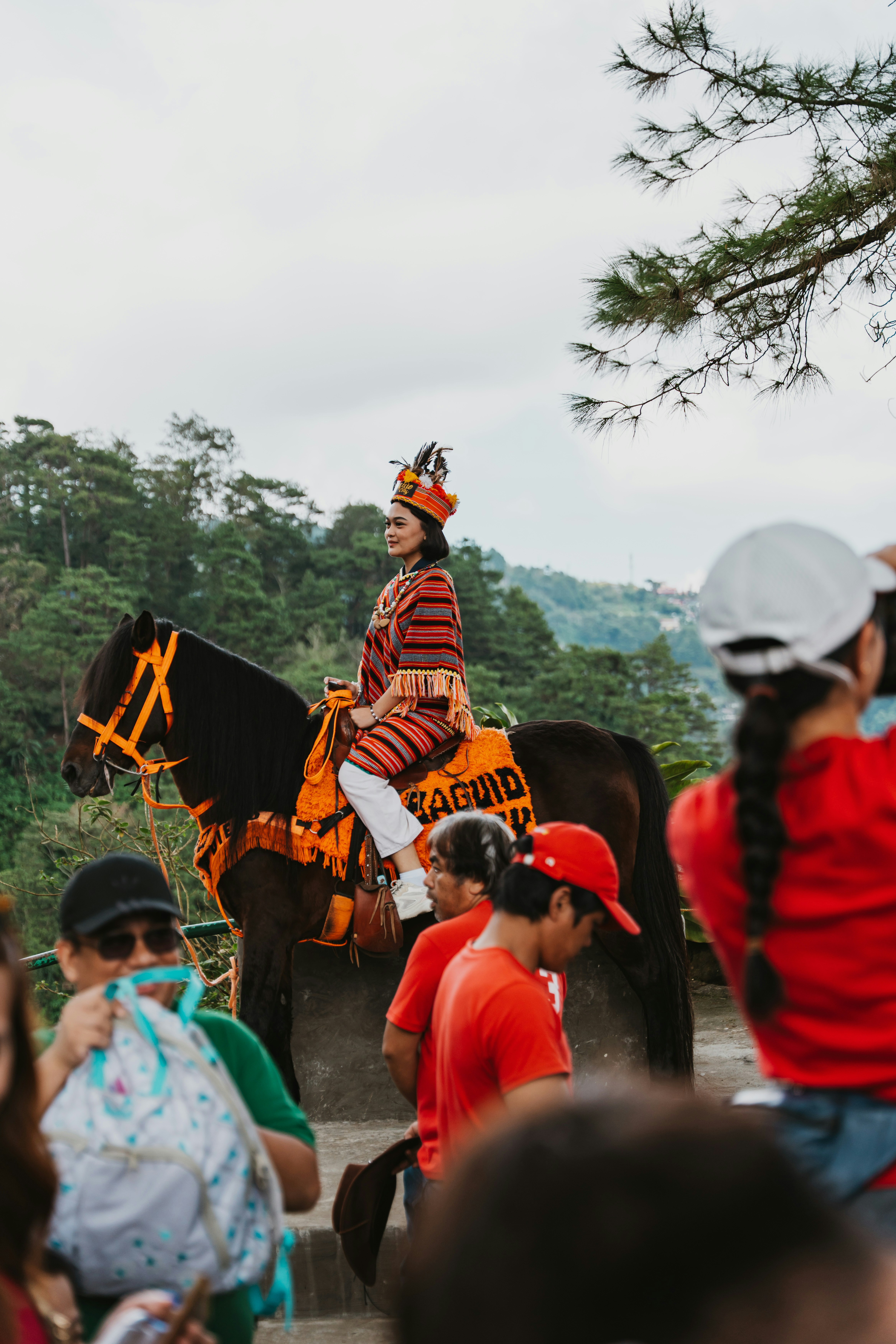 A woman in traditional woven clothing riding a horse among a crowd of people