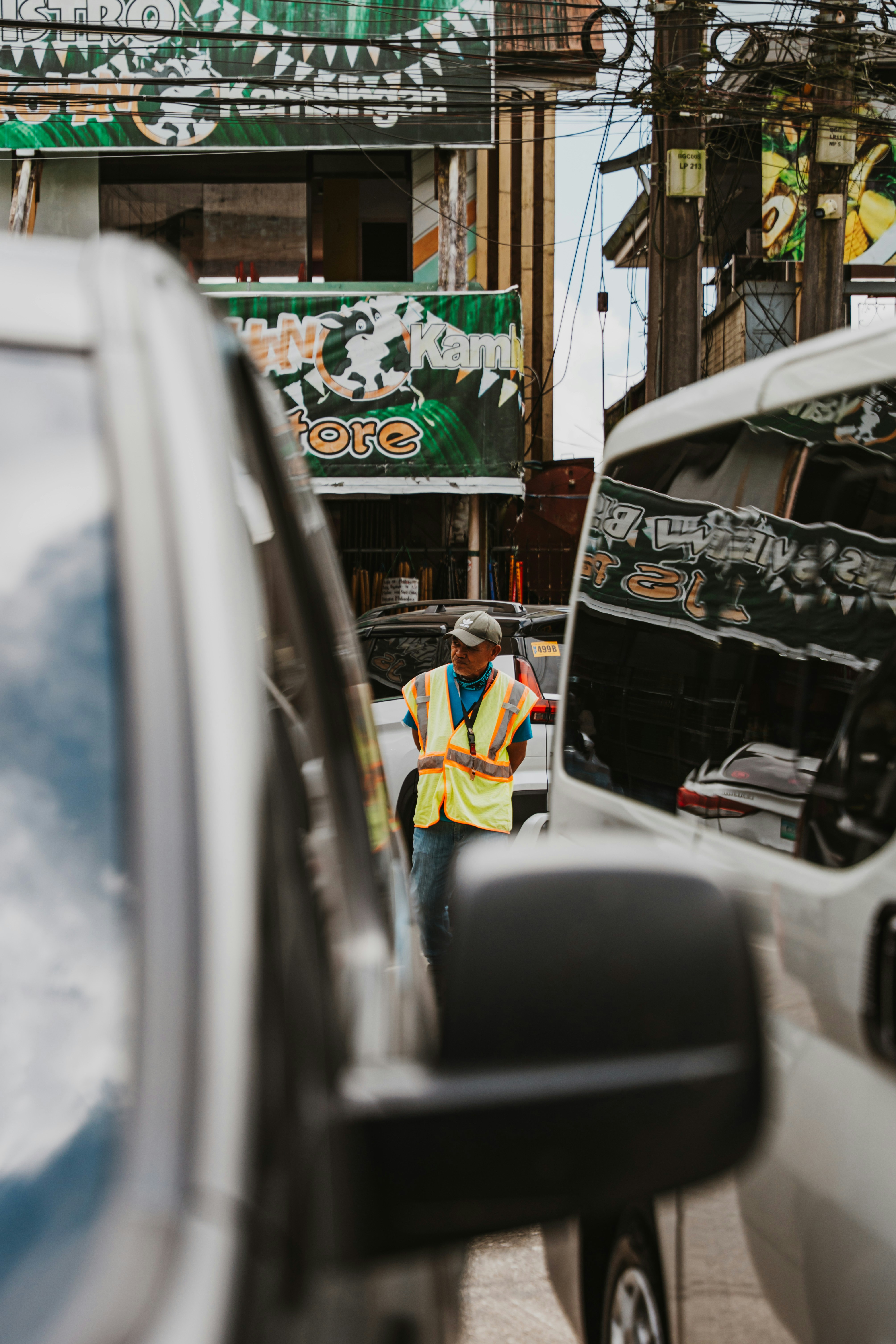 A traffic enforcer in a high-visibility vest standing between two white vehicles
