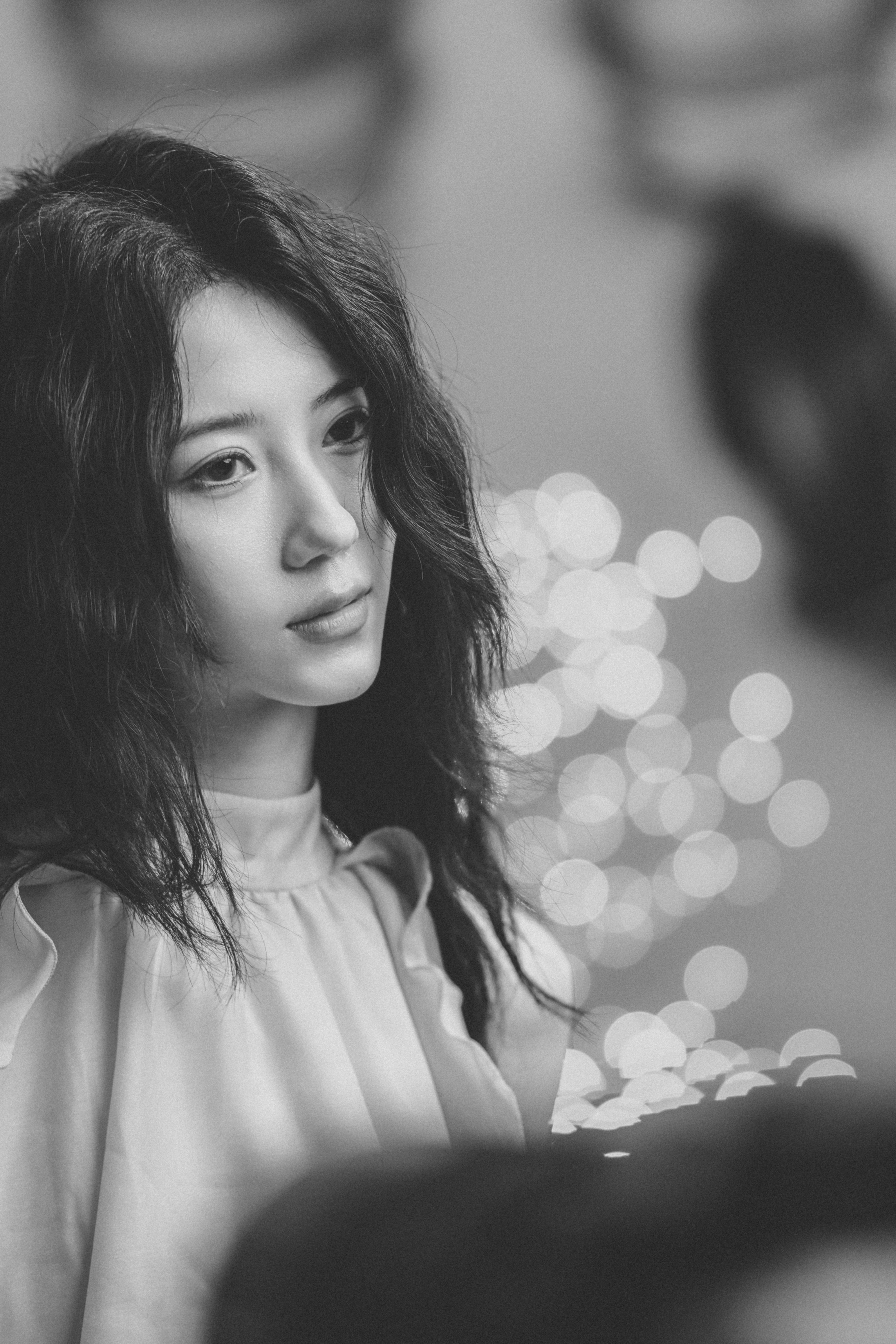 A woman with long dark hair in a ruffled top against bokeh lights