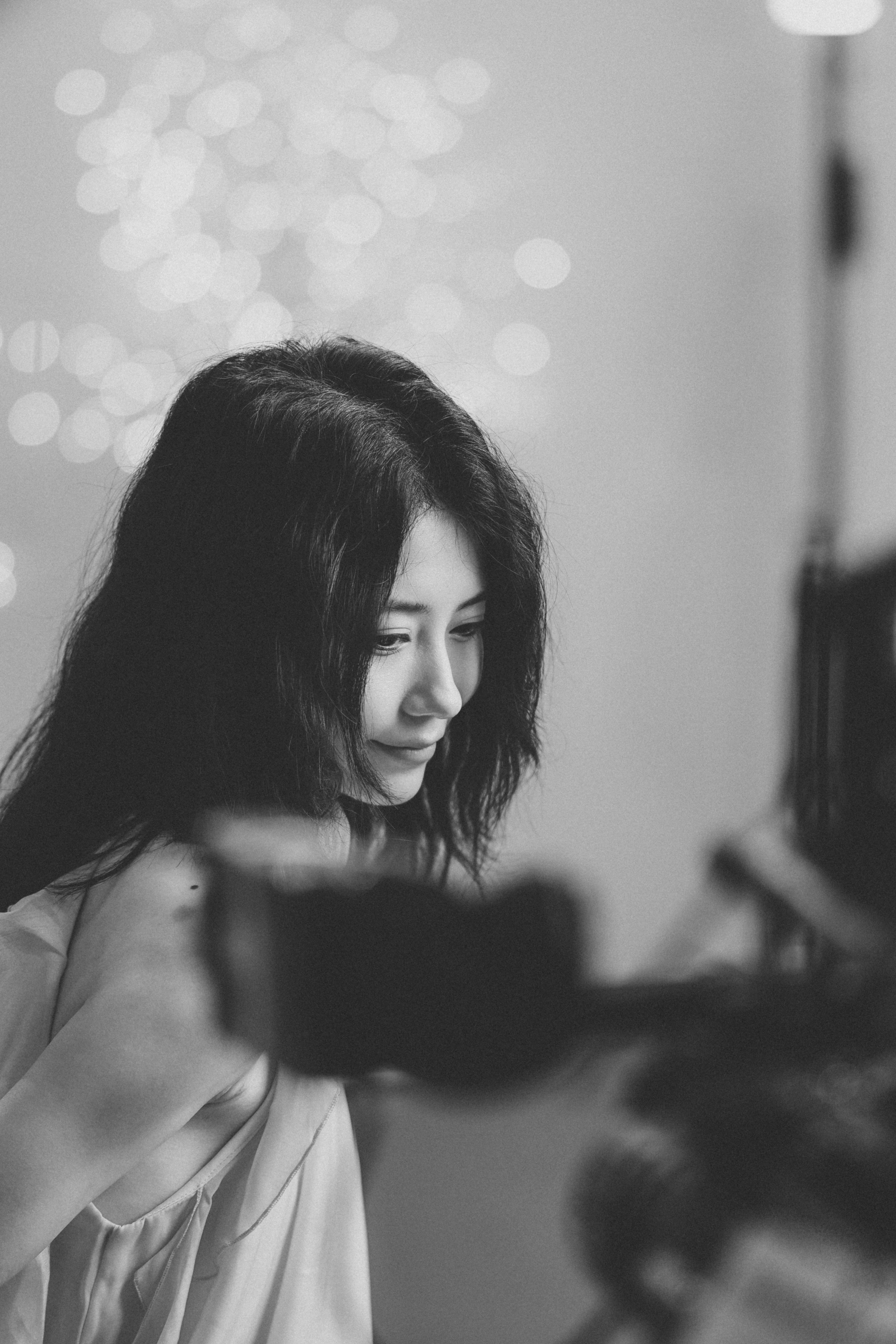 A woman with dark hair looking down against a background of soft bokeh lights