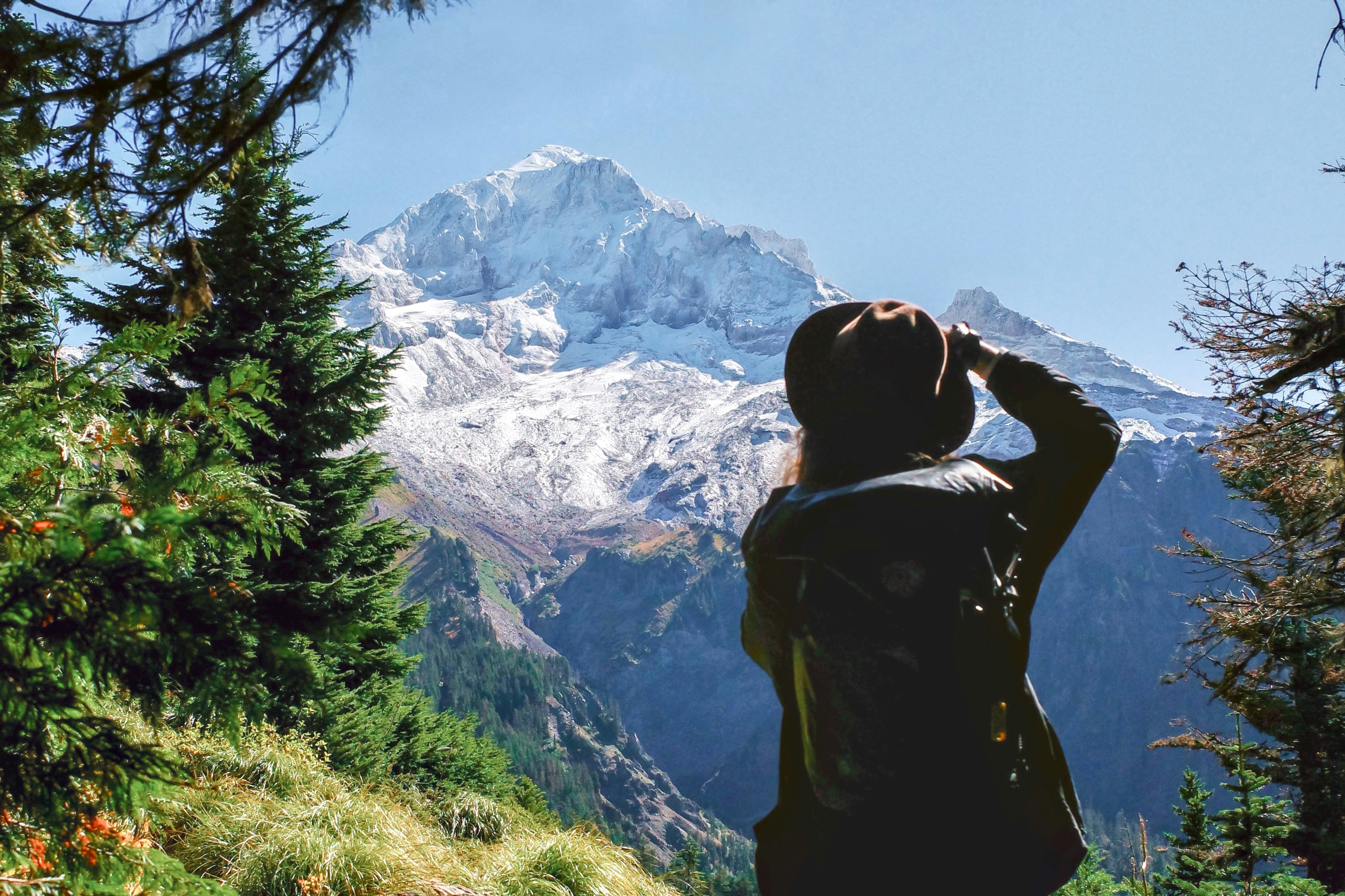 A person with a backpack and hat looking at a snow-capped mountain peak