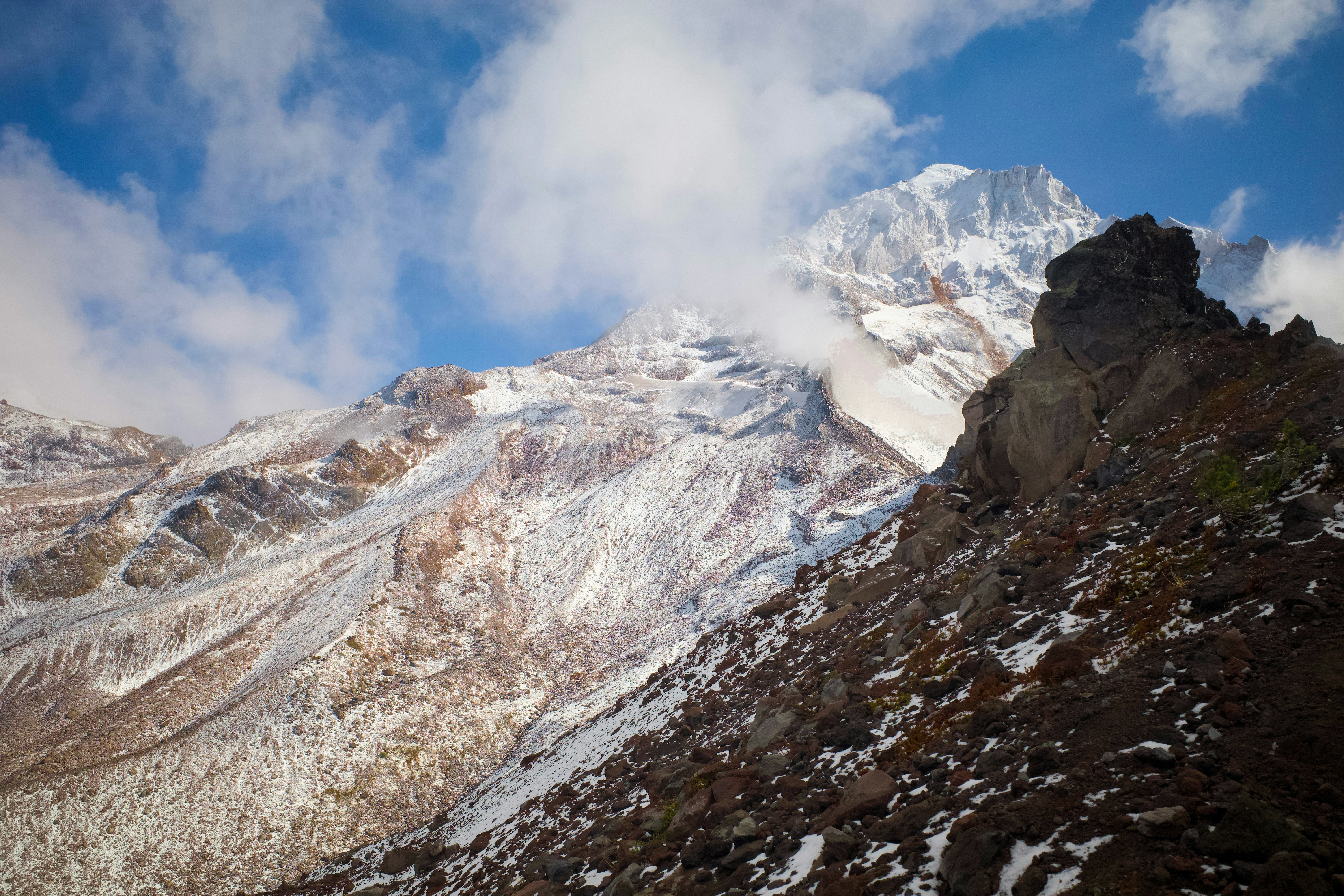 A snow-covered mountain peak rising above a rocky slope under a blue sky