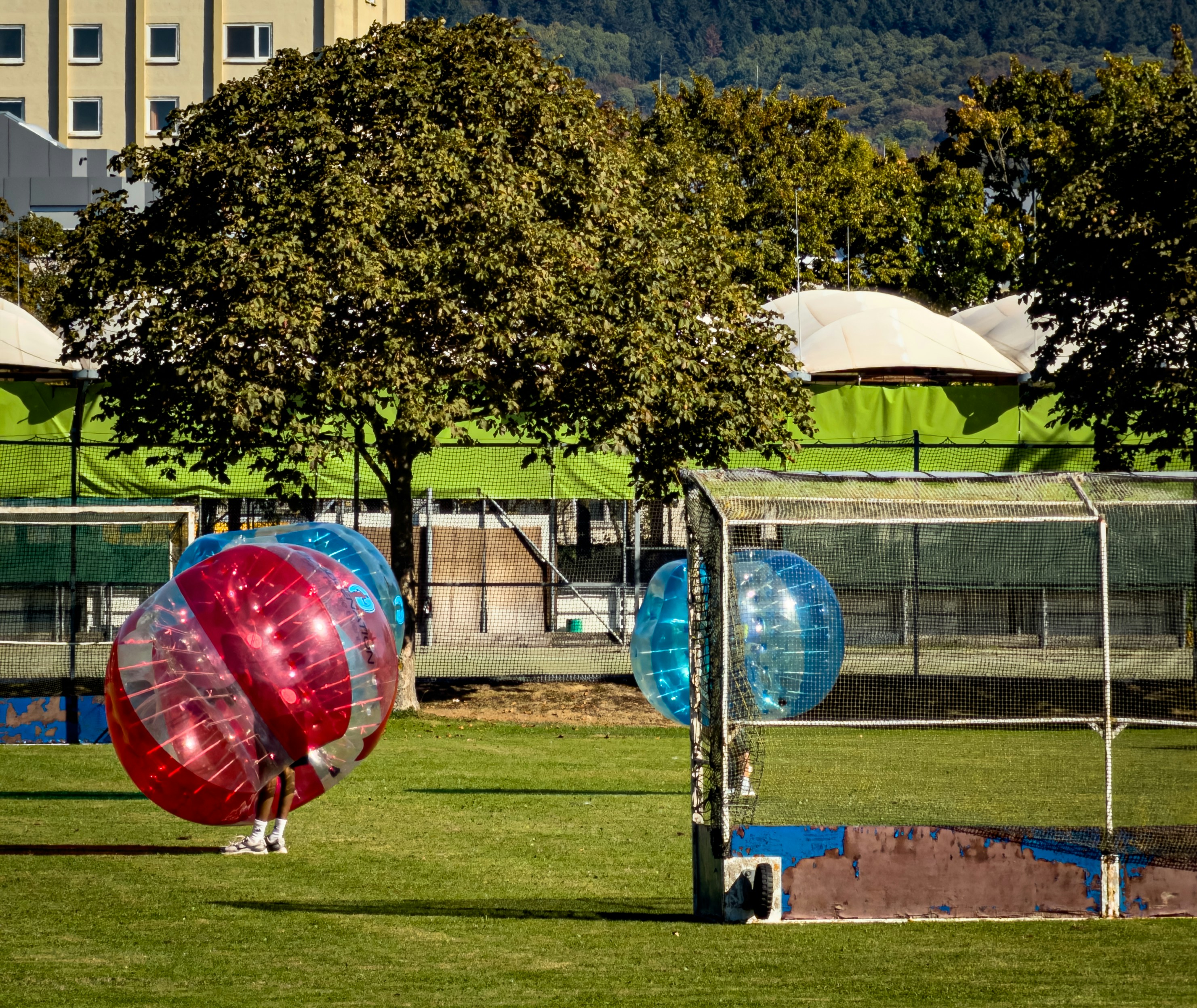 People in red and blue bubble suits playing soccer on a grassy field