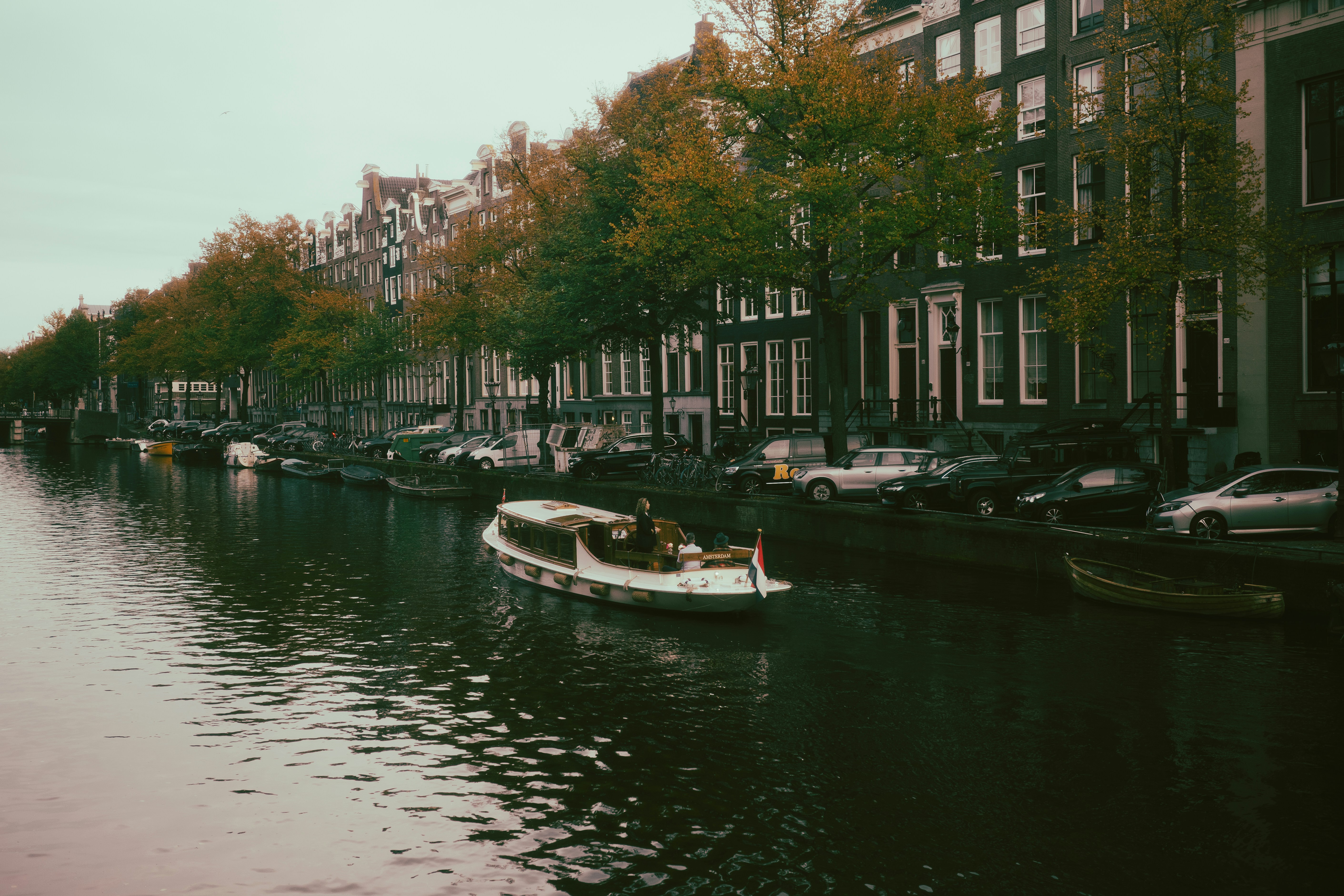 A canal boat cruising past historic buildings and parked cars in Amsterdam