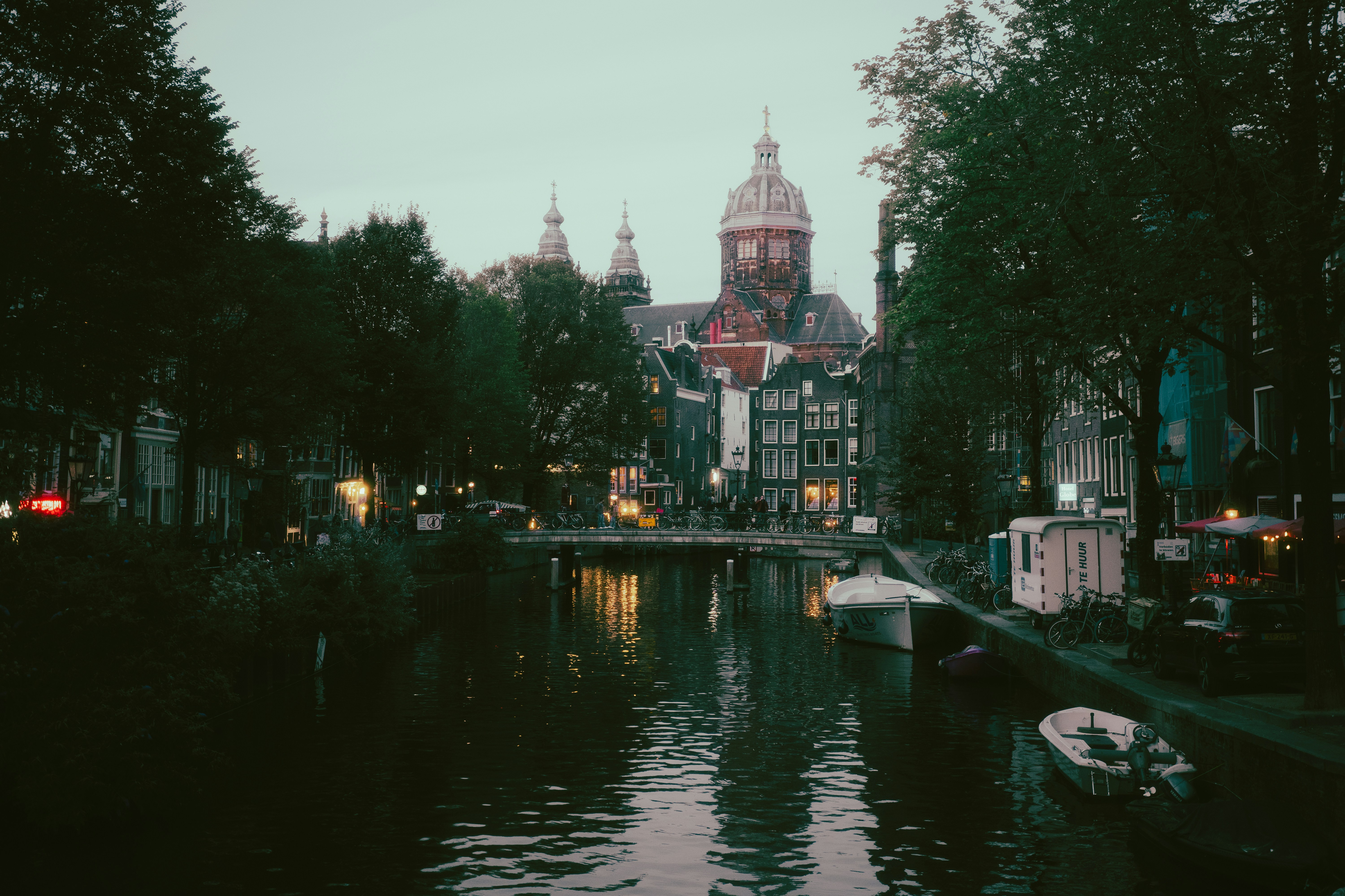 A canal in Amsterdam with boats moored along the bank and a domed church