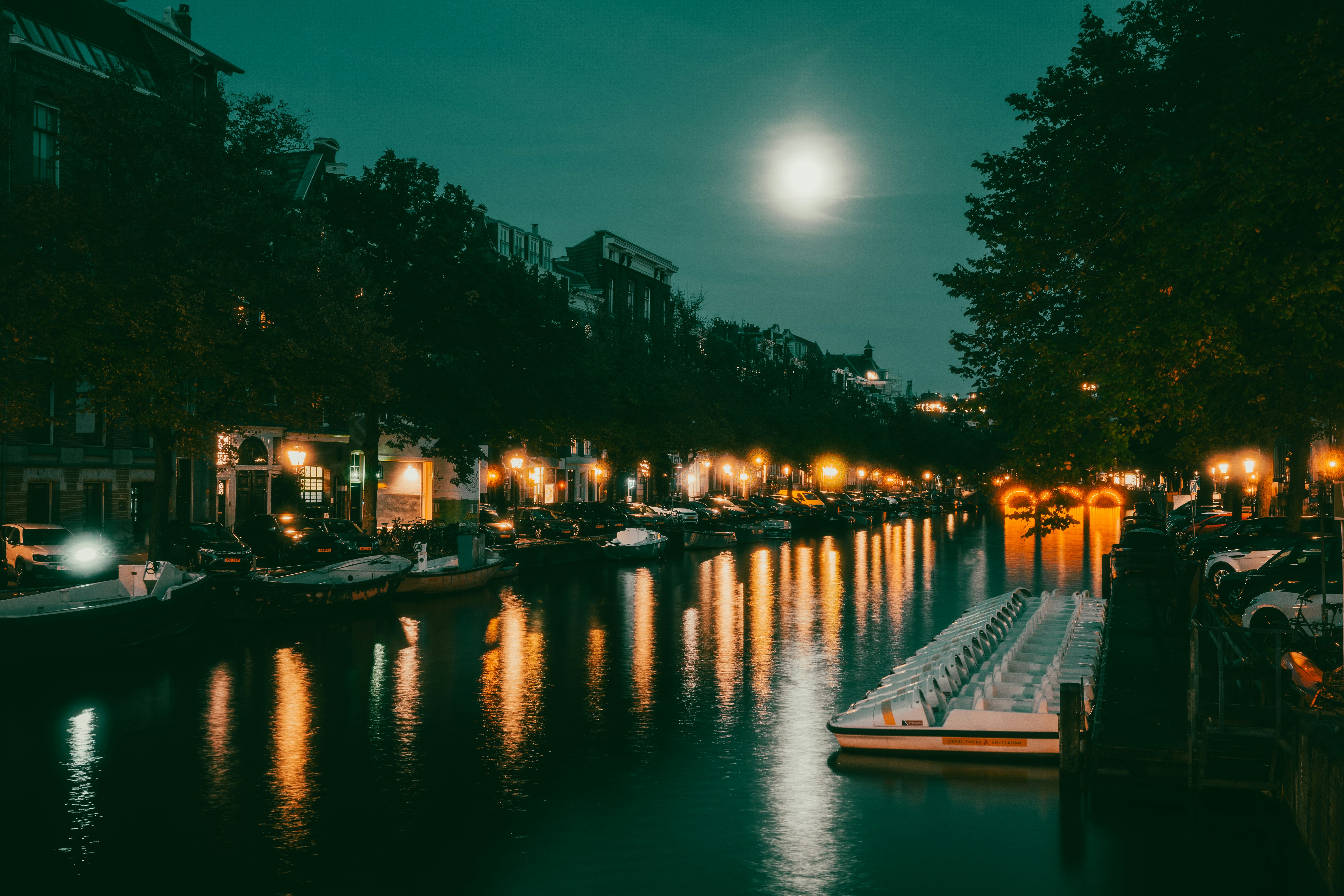 A canal in Amsterdam at night with streetlights reflecting on the dark water
