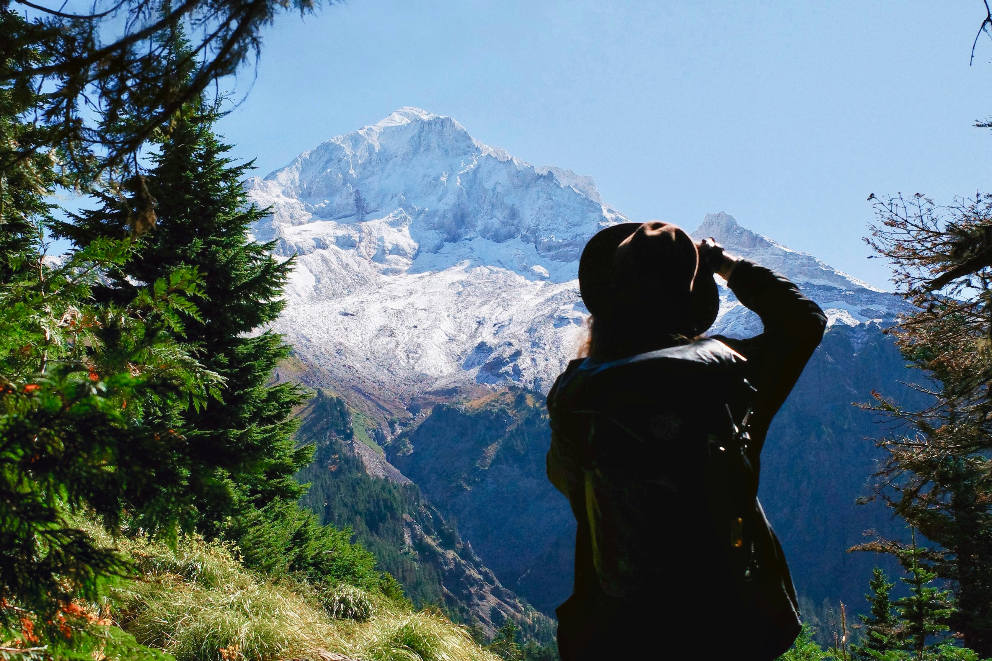 A person in a hat and backpack looking at a snow-capped mountain peak