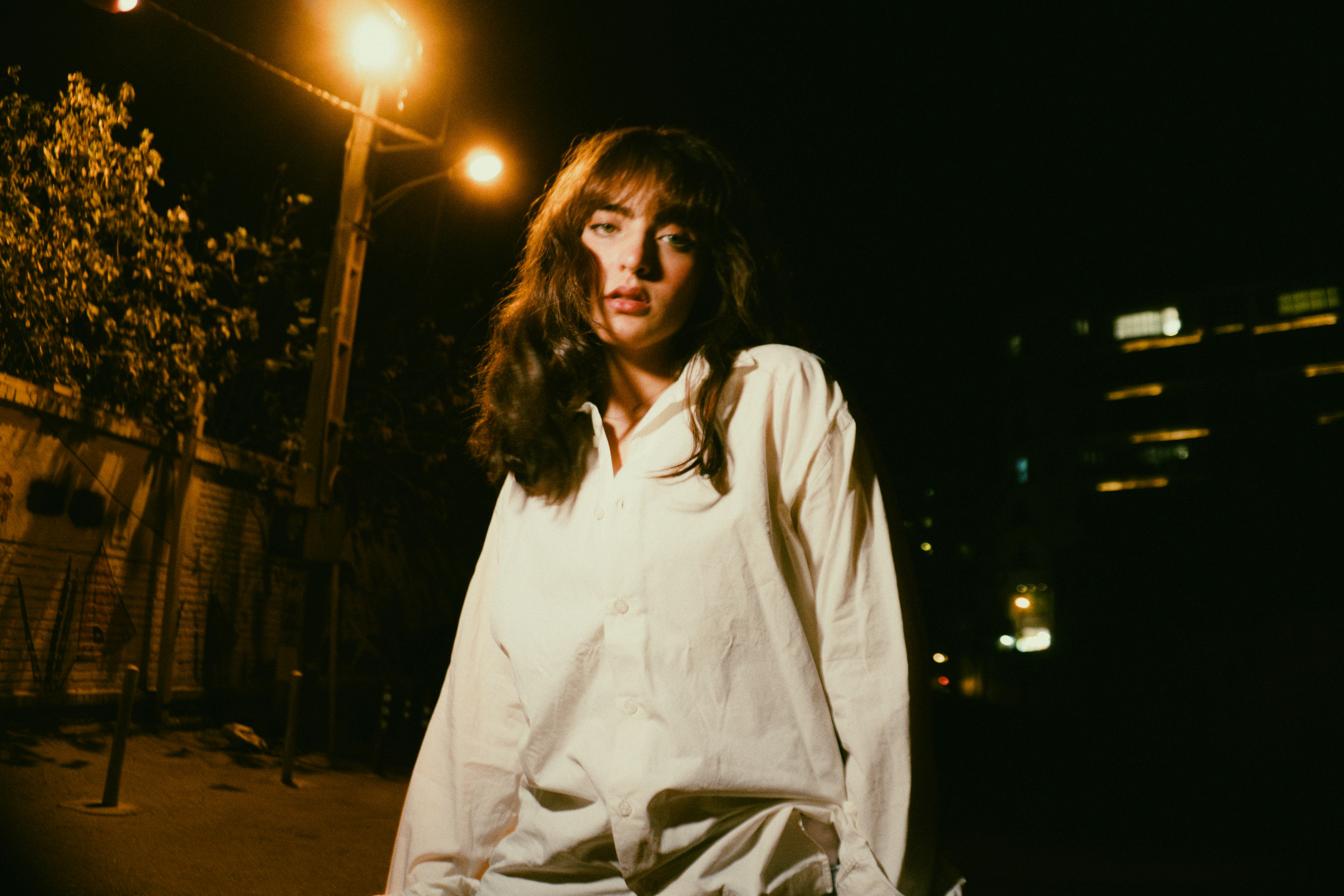 A woman in a white button-down shirt standing on a street at night