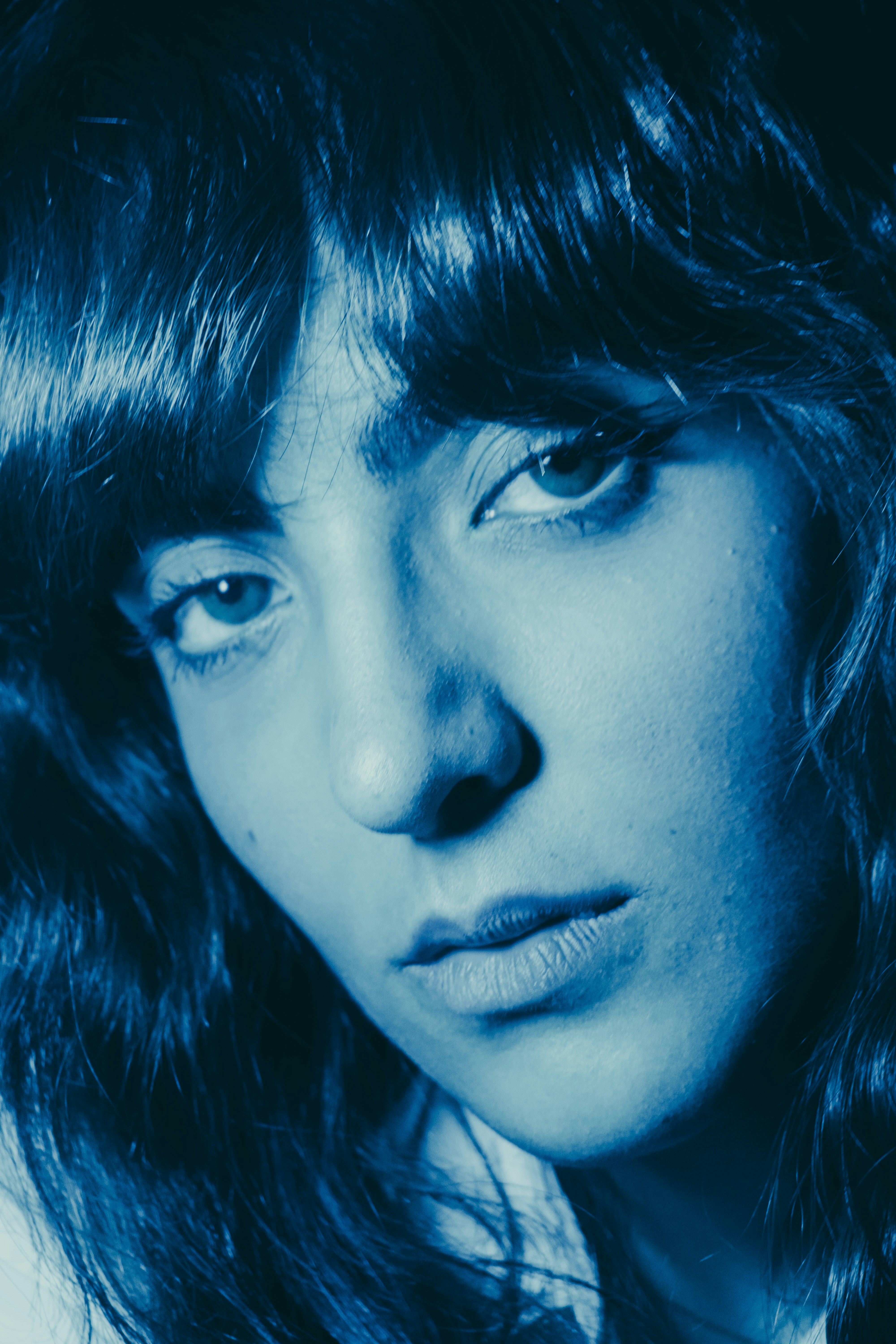 A close-up portrait of a person with long dark hair in blue light