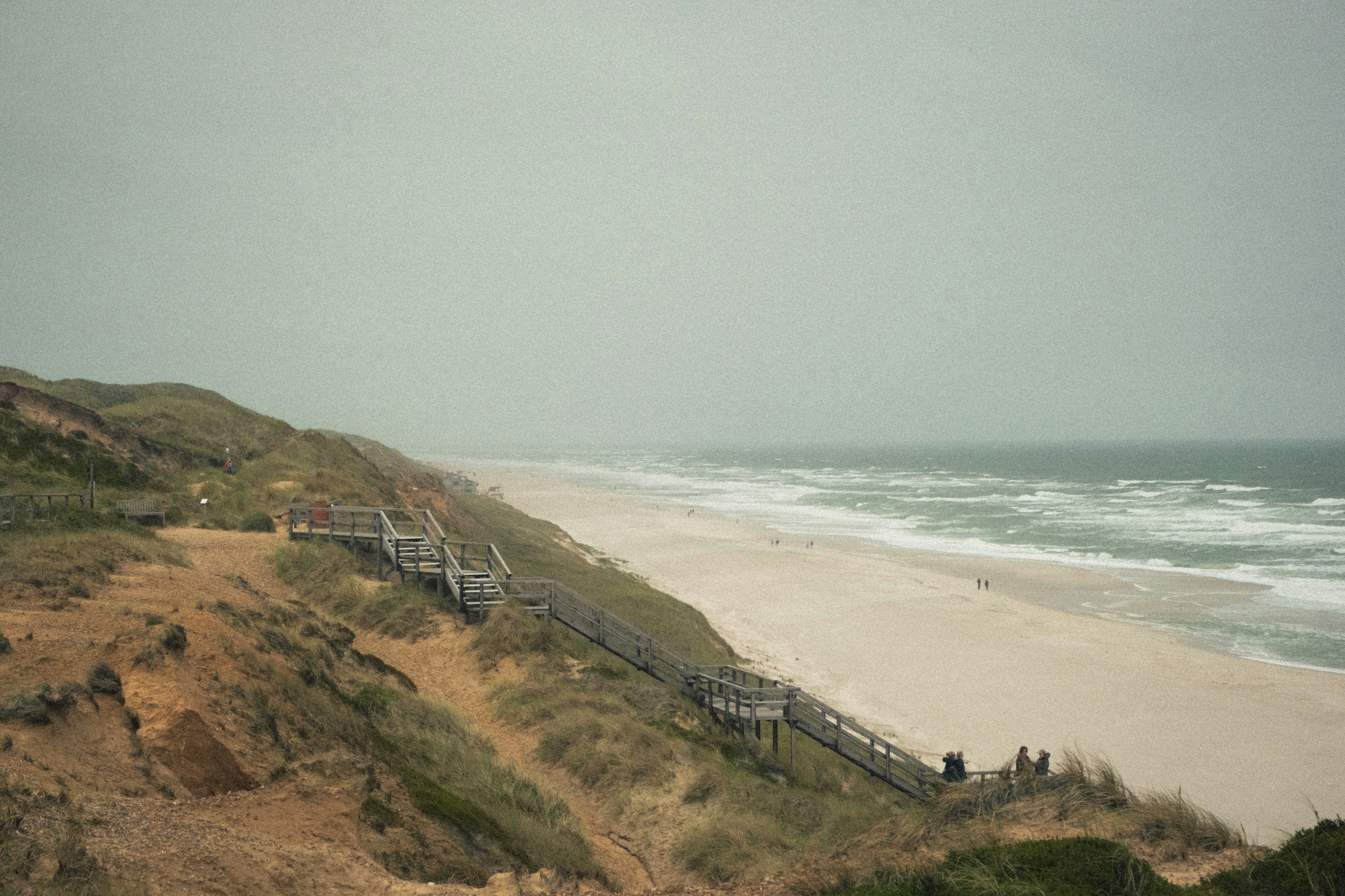 Wooden stairs descending a grassy dune to a sandy beach with crashing waves
