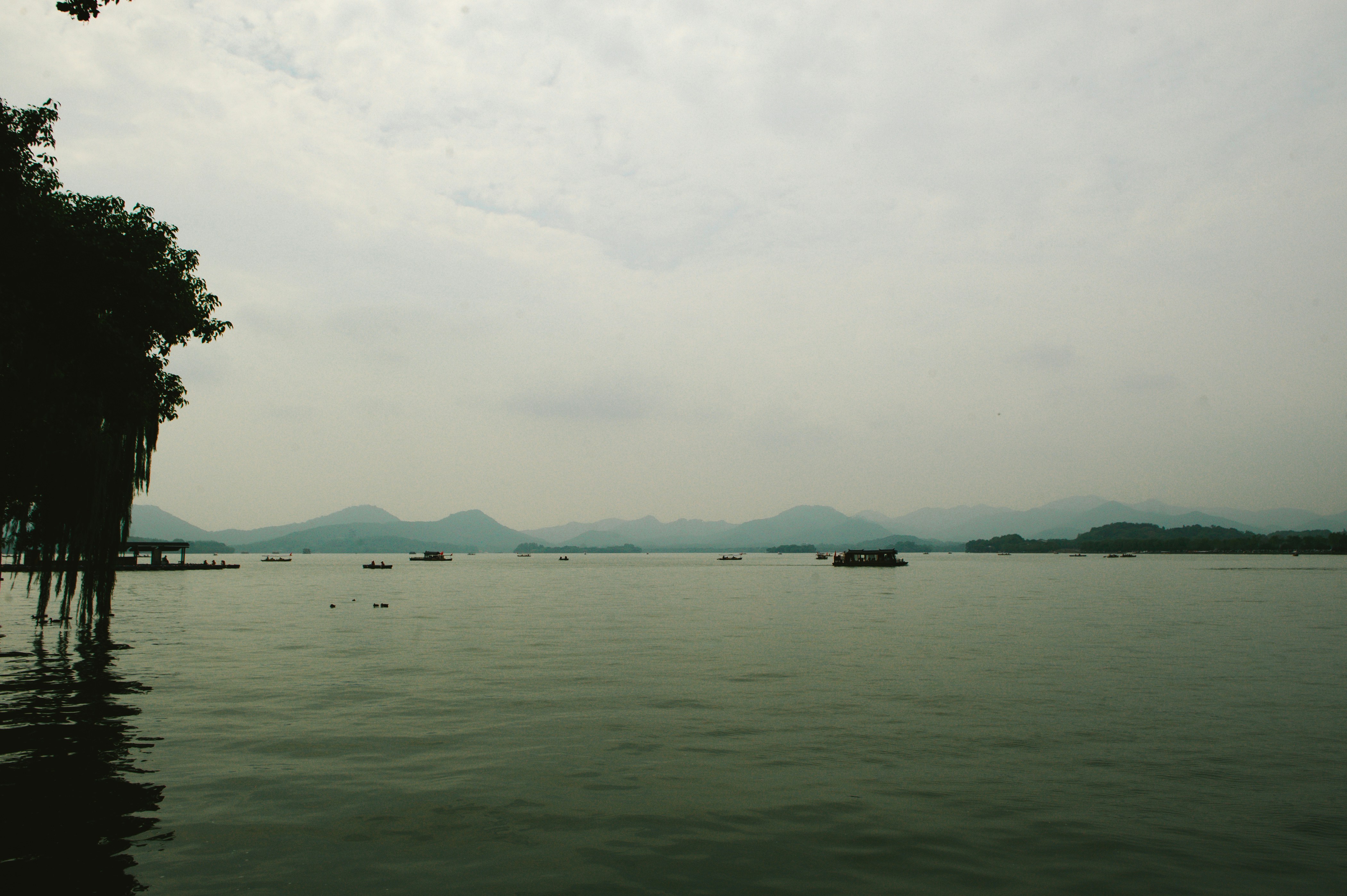 Small boats on a calm lake with distant mountains under a cloudy sky