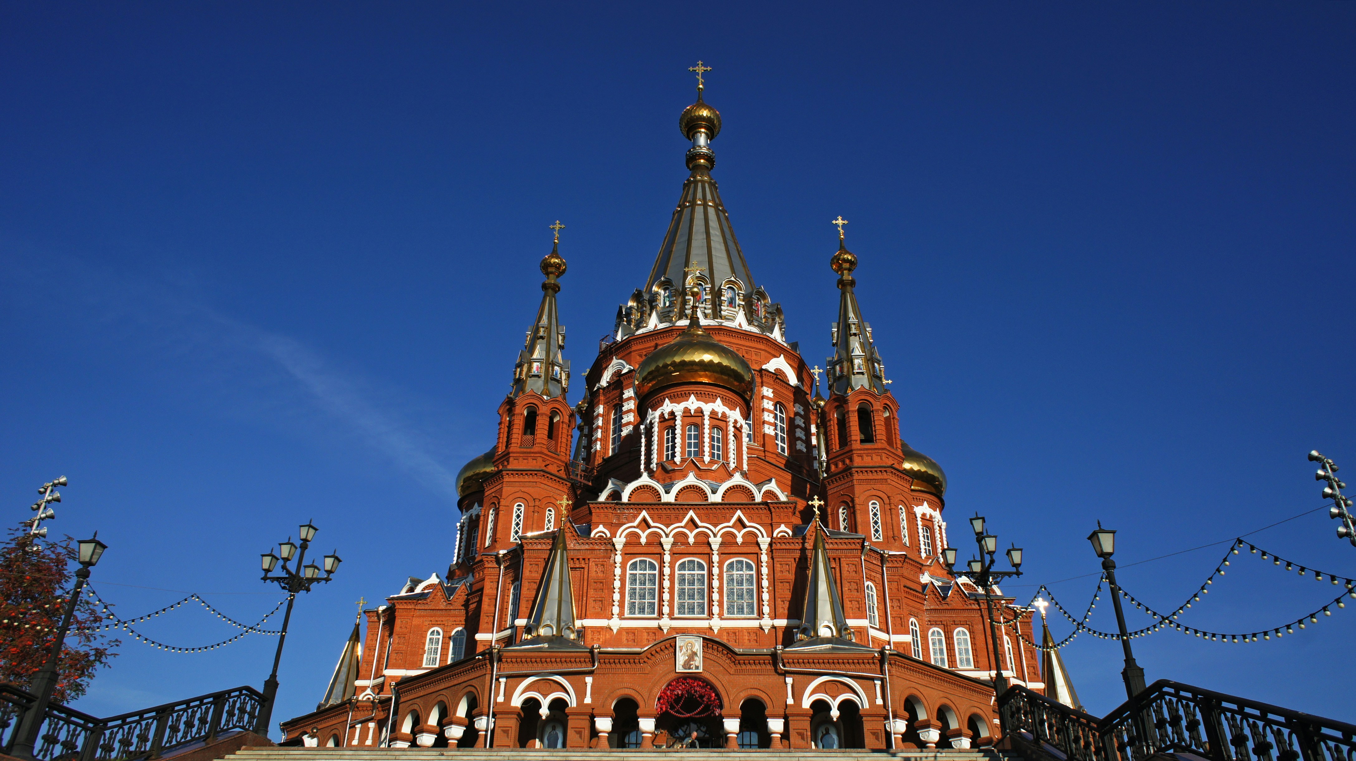 A red brick cathedral with golden domes against a clear deep blue sky