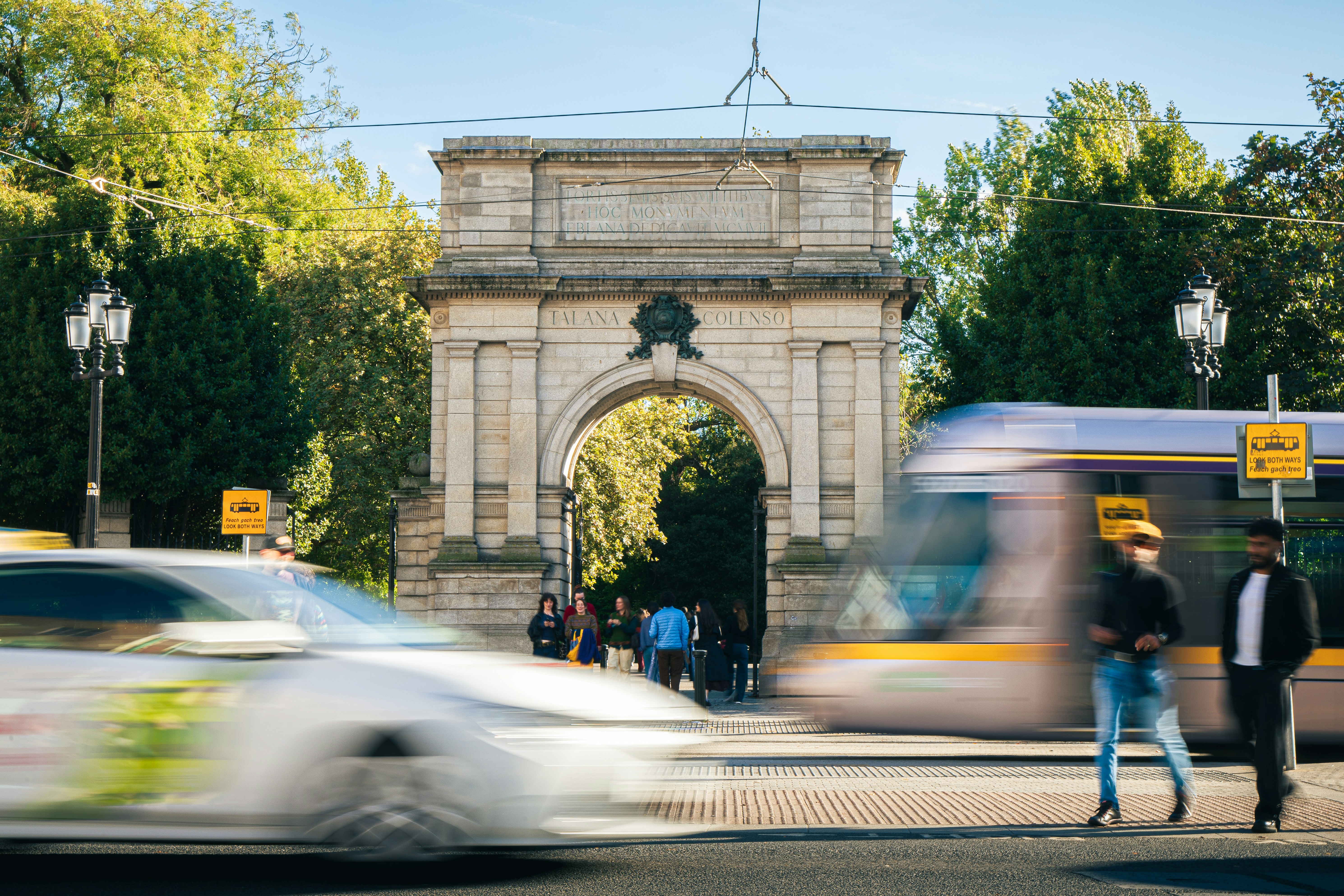 A stone archway in Dublin with a blurred tram and car passing by