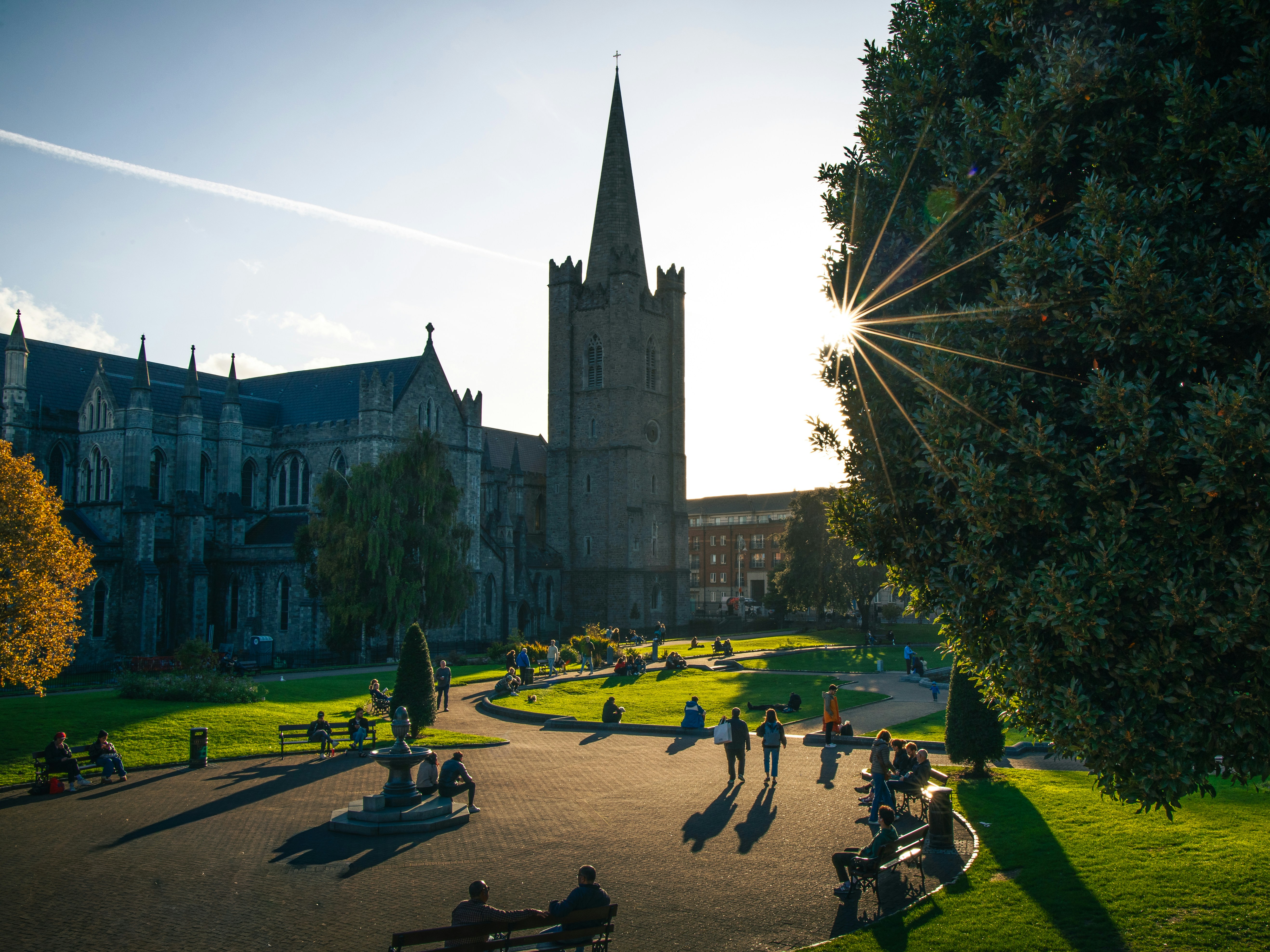 People relaxing in a park beside St Patrick's Cathedral in Dublin at golden hour