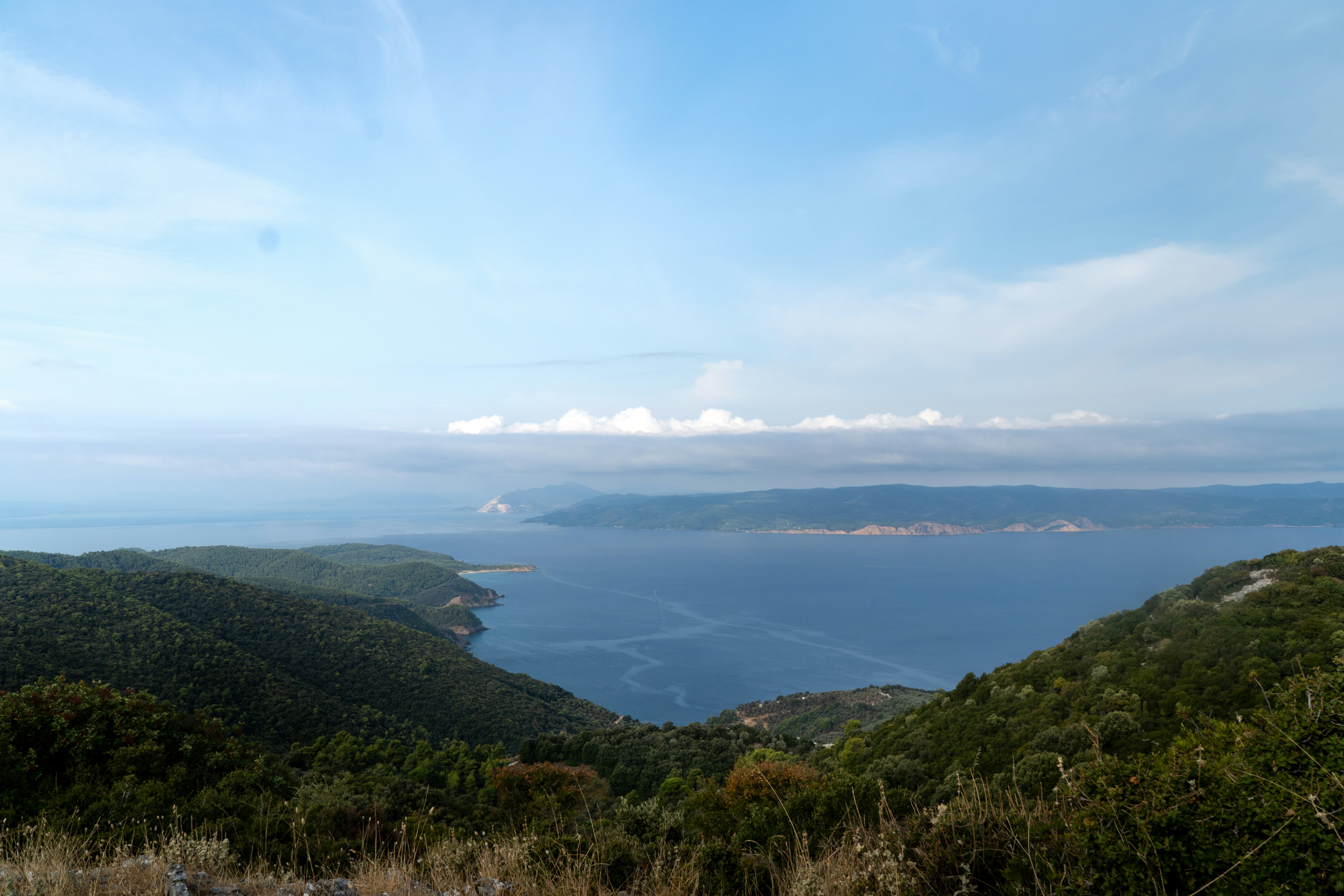 A wide view of a deep blue bay surrounded by green forested hills