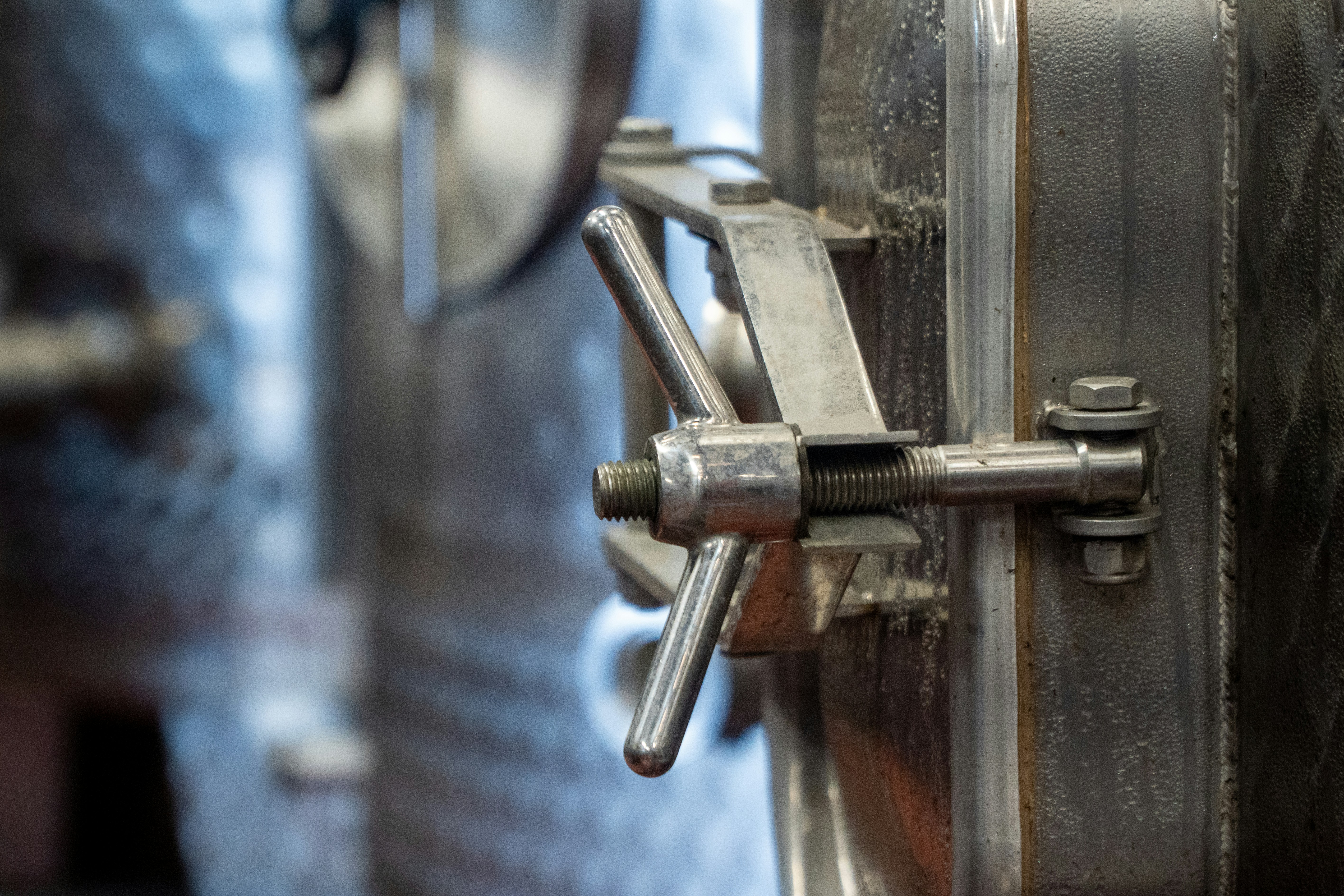 A metal wing nut fastener on a stainless steel industrial tank door