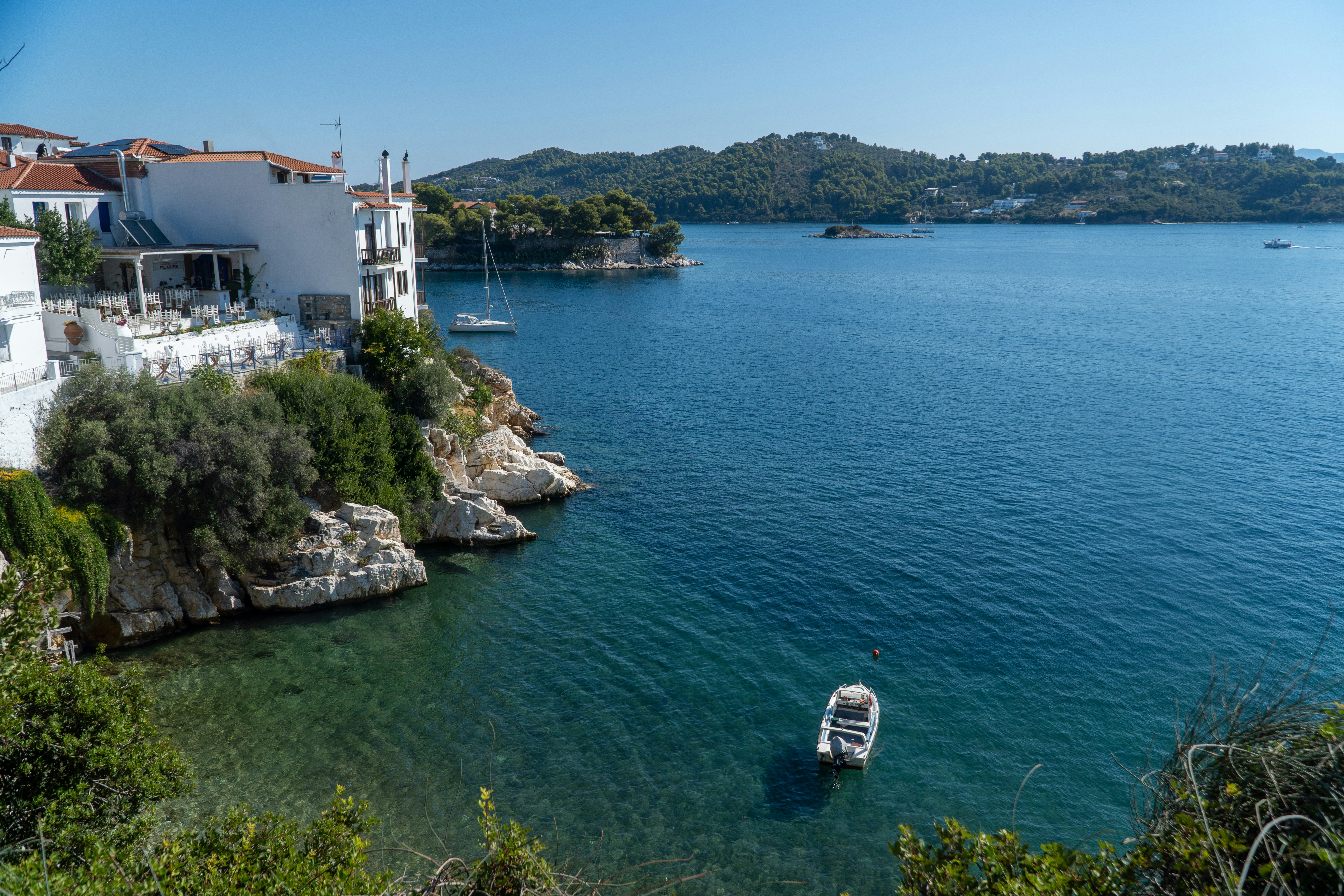 White buildings on a rocky cliff overlooking a blue bay with small boats