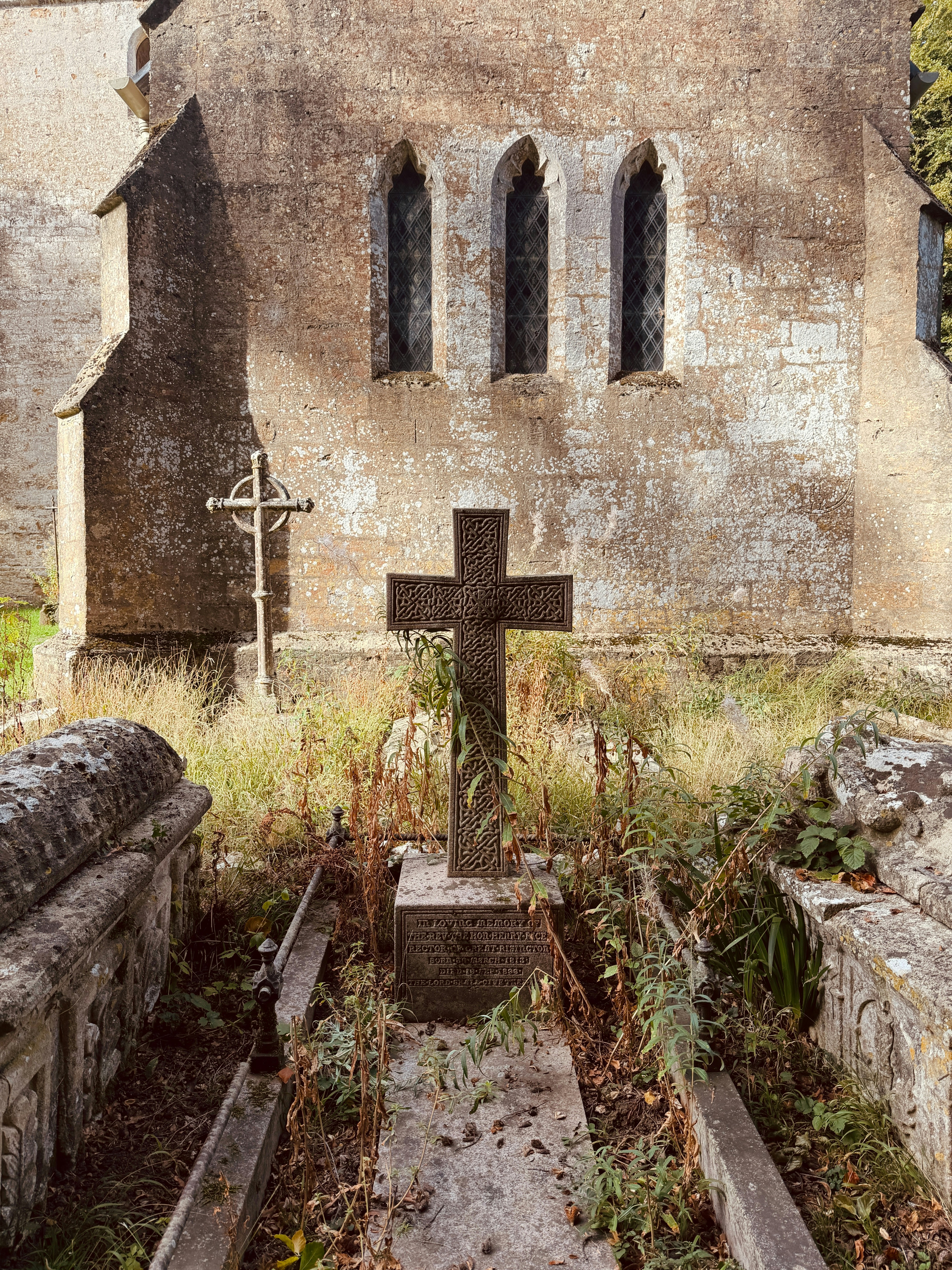 A stone cross on a grave in front of an old stone church
