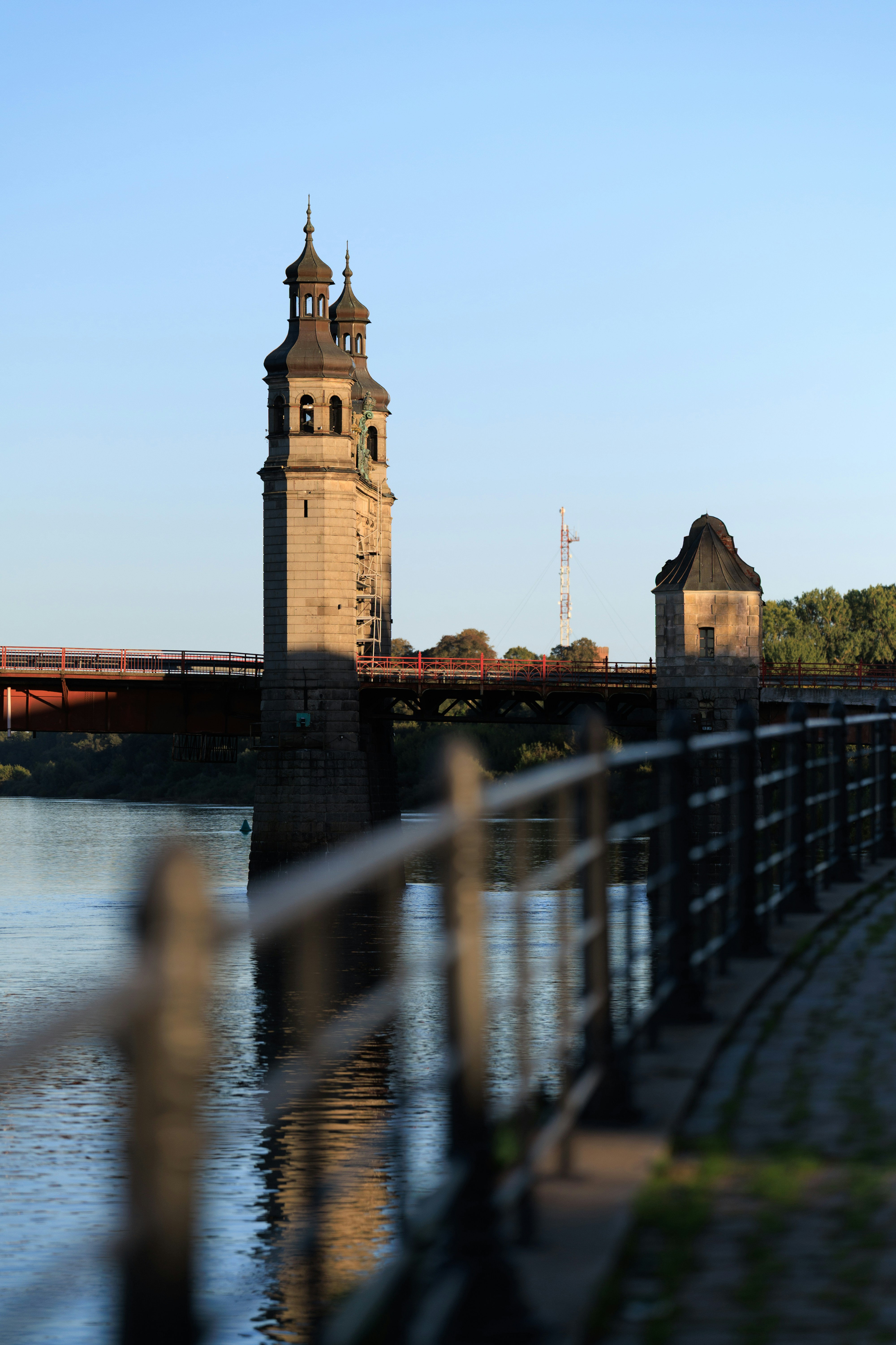 A stone bridge with tall towers spanning a river at golden hour