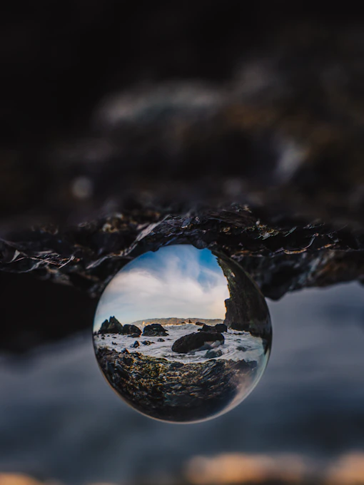 A coastal landscape reflected in a glass sphere held against dark jagged rocks