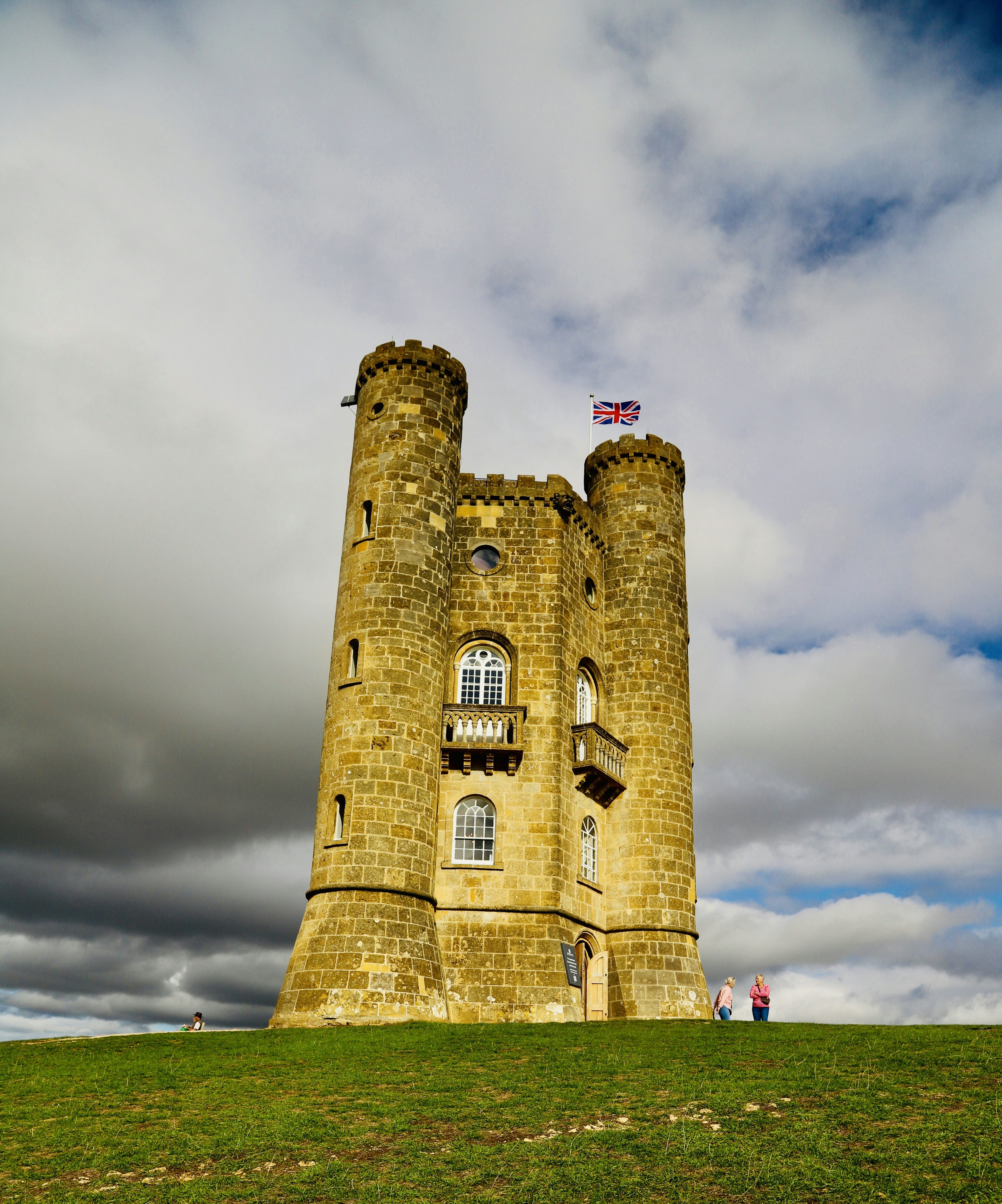 Broadway Tower with a British flag on a grassy hill under cloudy skies