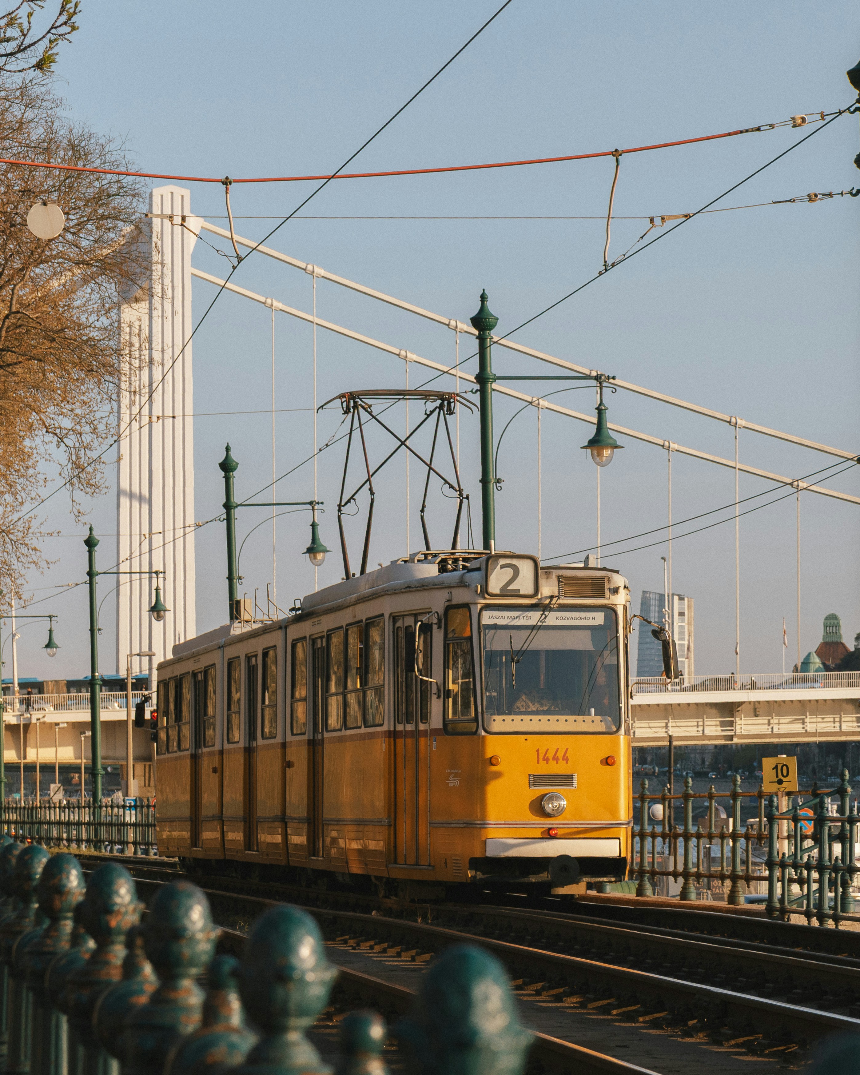 A yellow tram on tracks near the white pylon of the Elizabeth Bridge in Budapest
