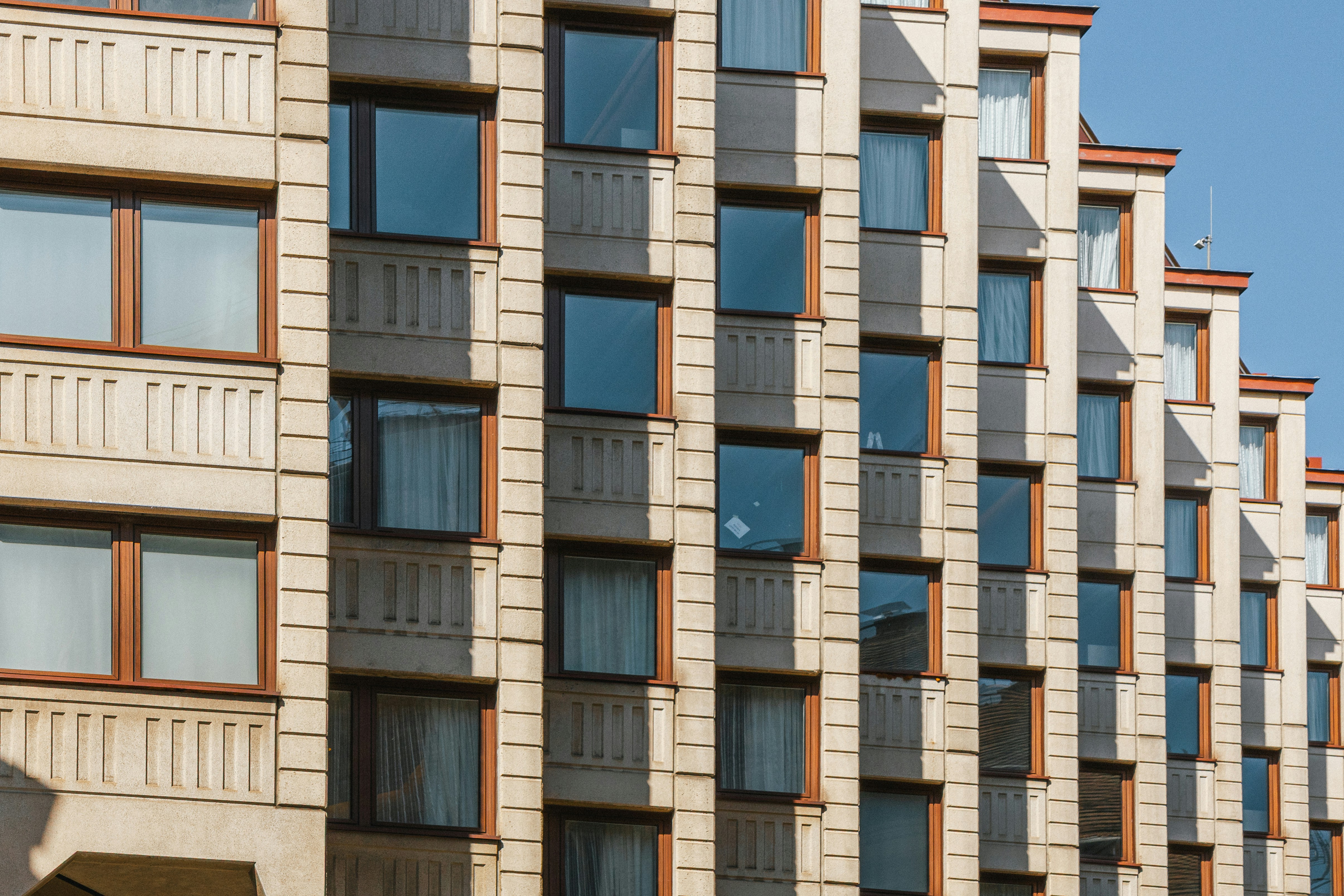 A modern building facade with repeating concrete panels and recessed windows in sunlight