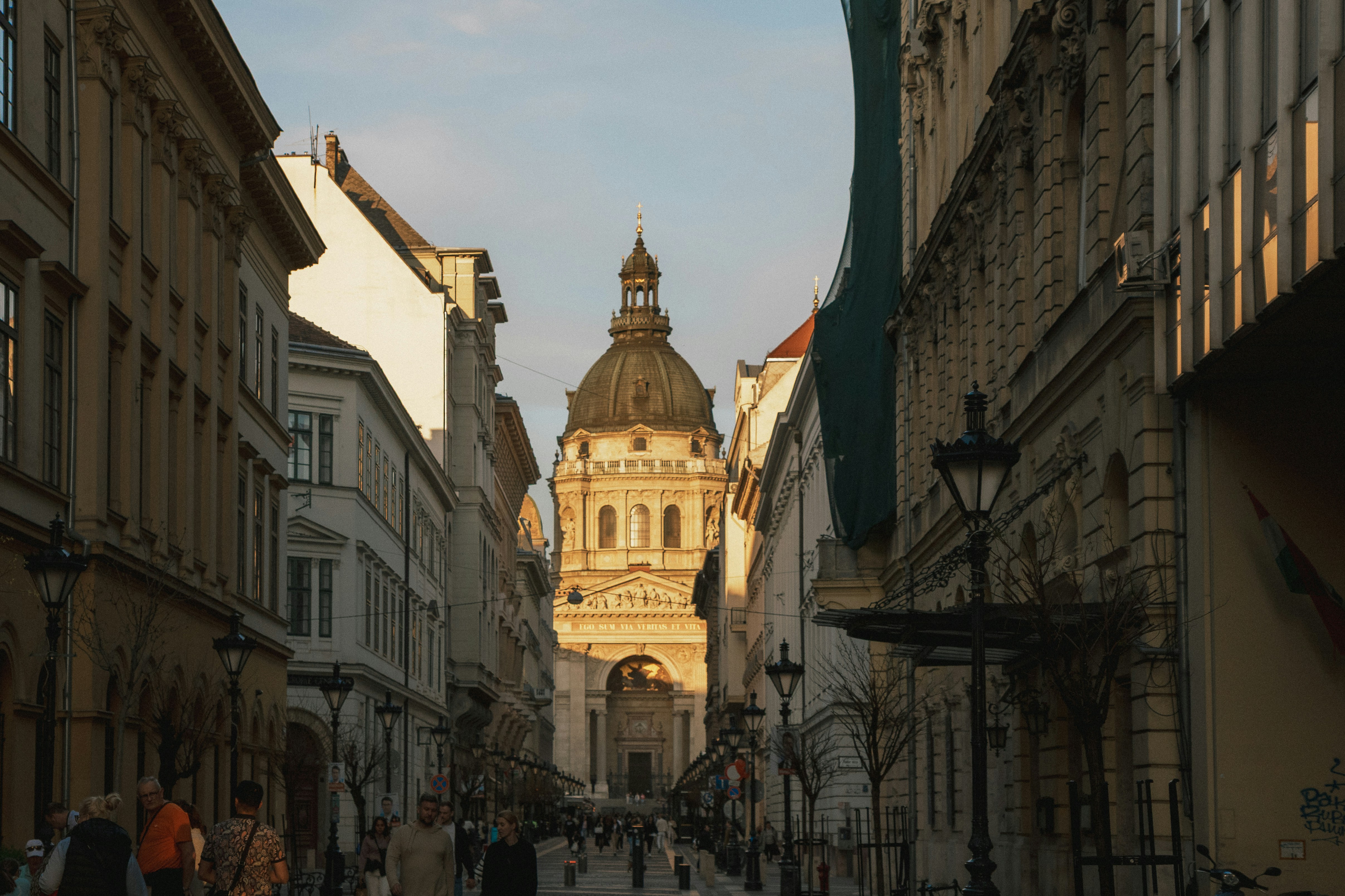People walking on a street toward St. Stephen's Basilica in Budapest at golden hour