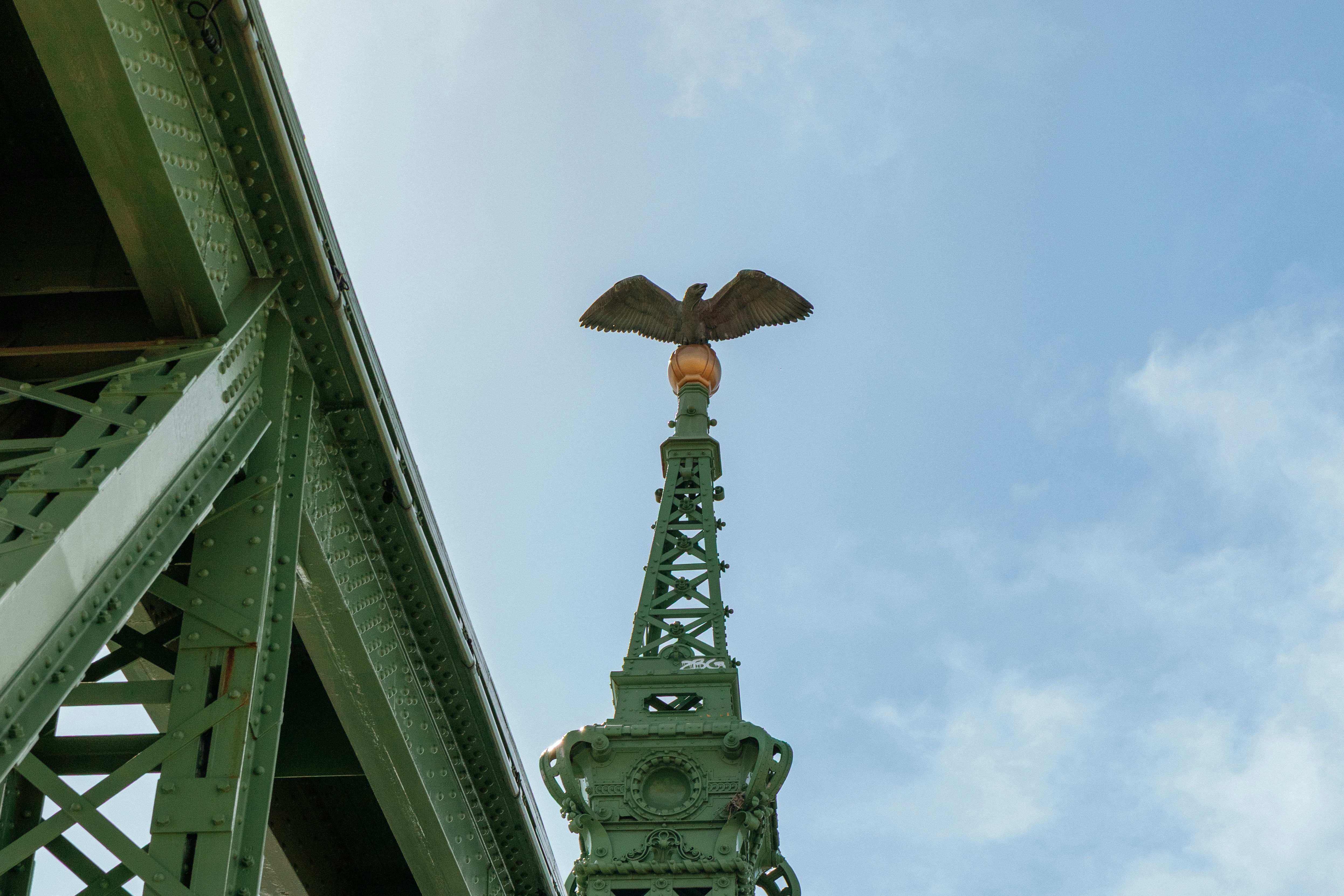 A bronze eagle statue atop a green metal spire against a blue sky