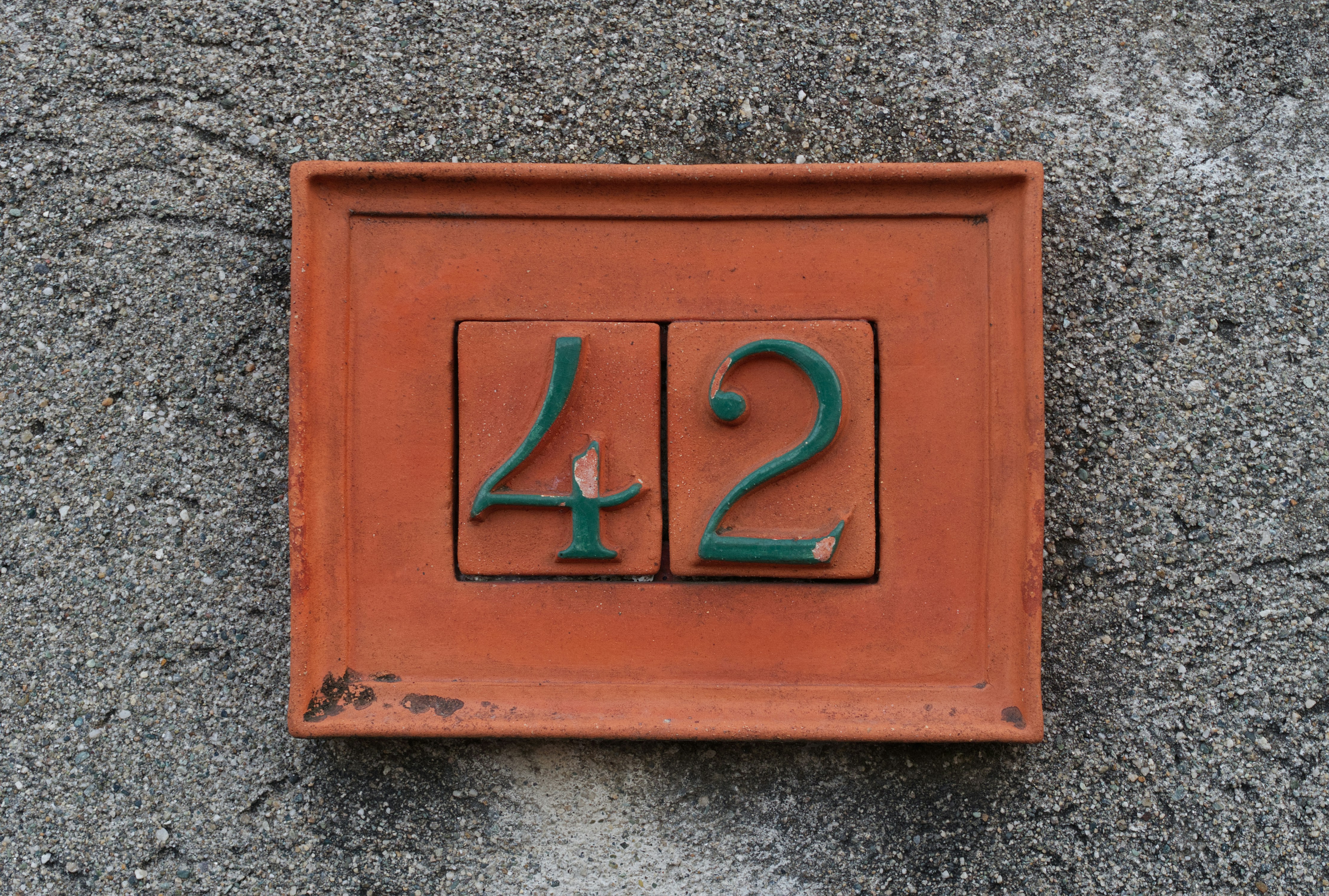 A terracotta plaque with the green number 42 on a grey concrete wall