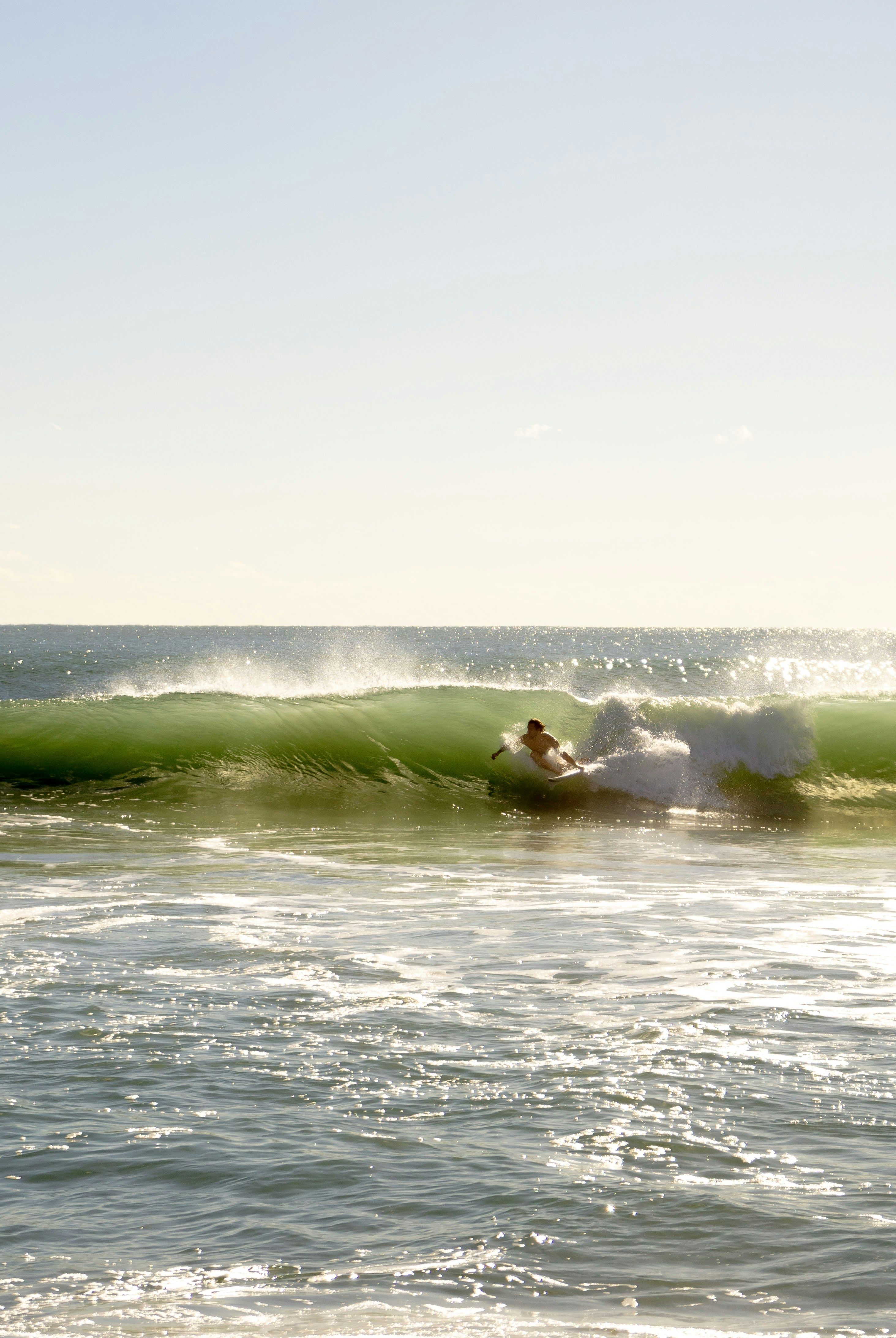A surfer riding a green wave in the ocean under bright low sun