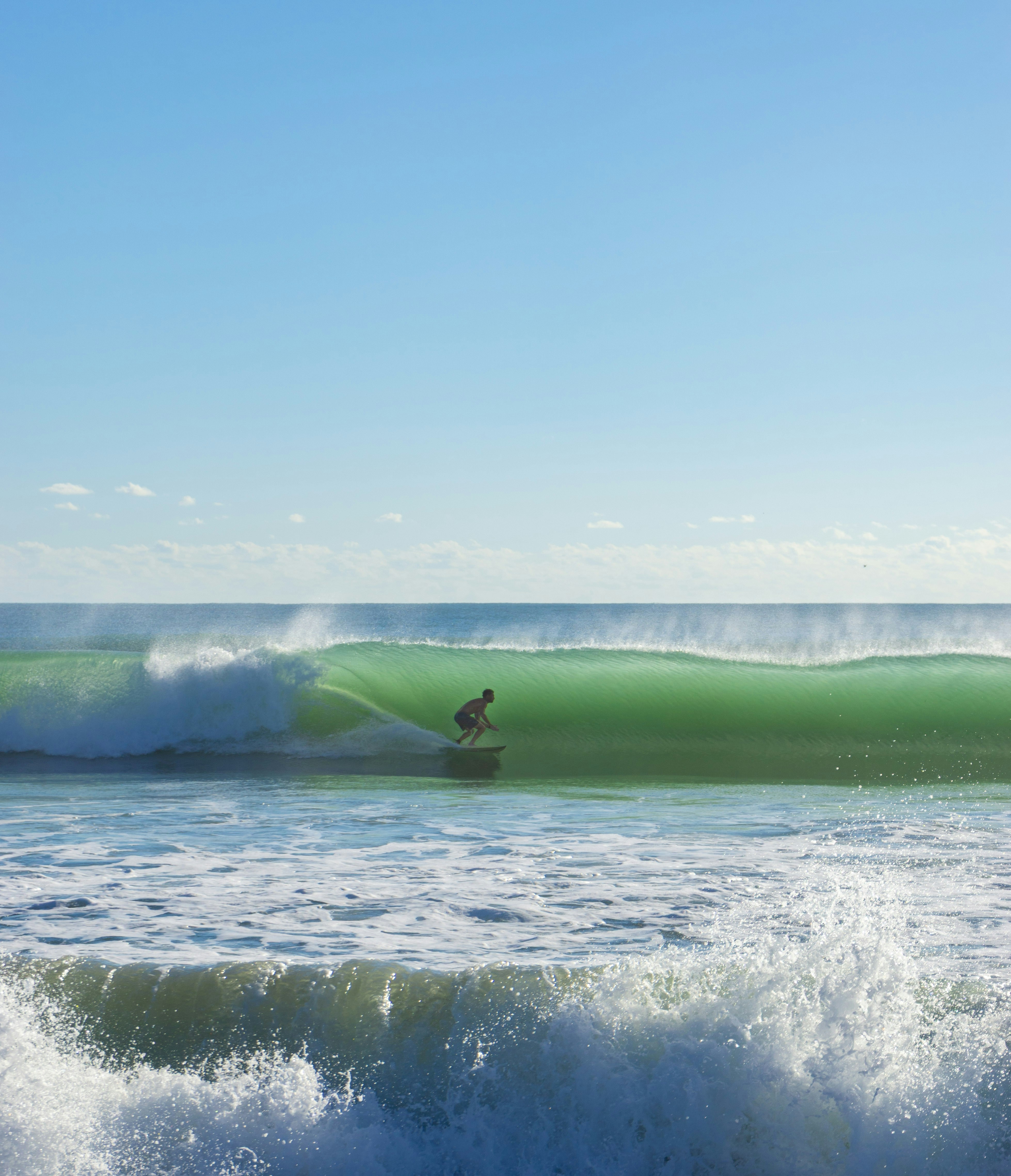 A surfer riding a green barrel wave under a clear blue sky