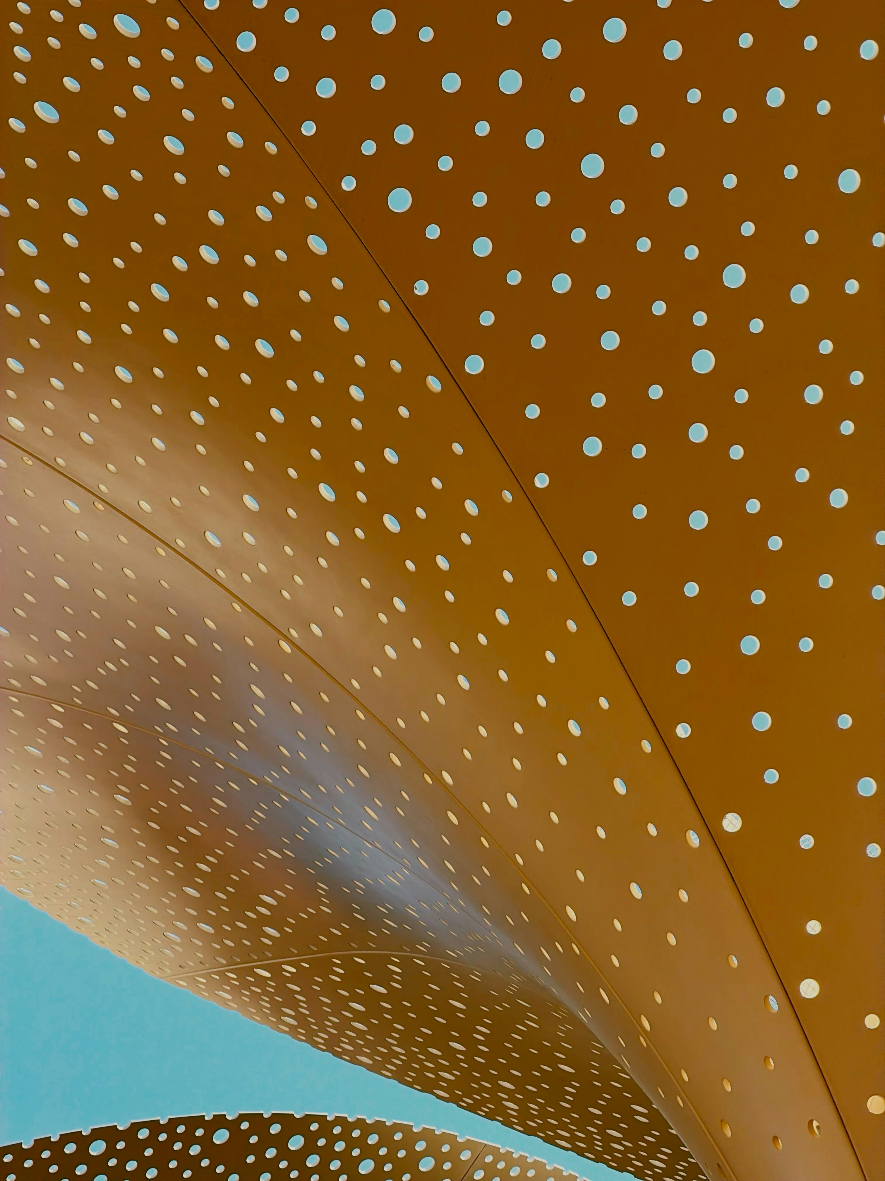 Un pannello giallo curvo con forature circolari contro un cielo azzurro limpido