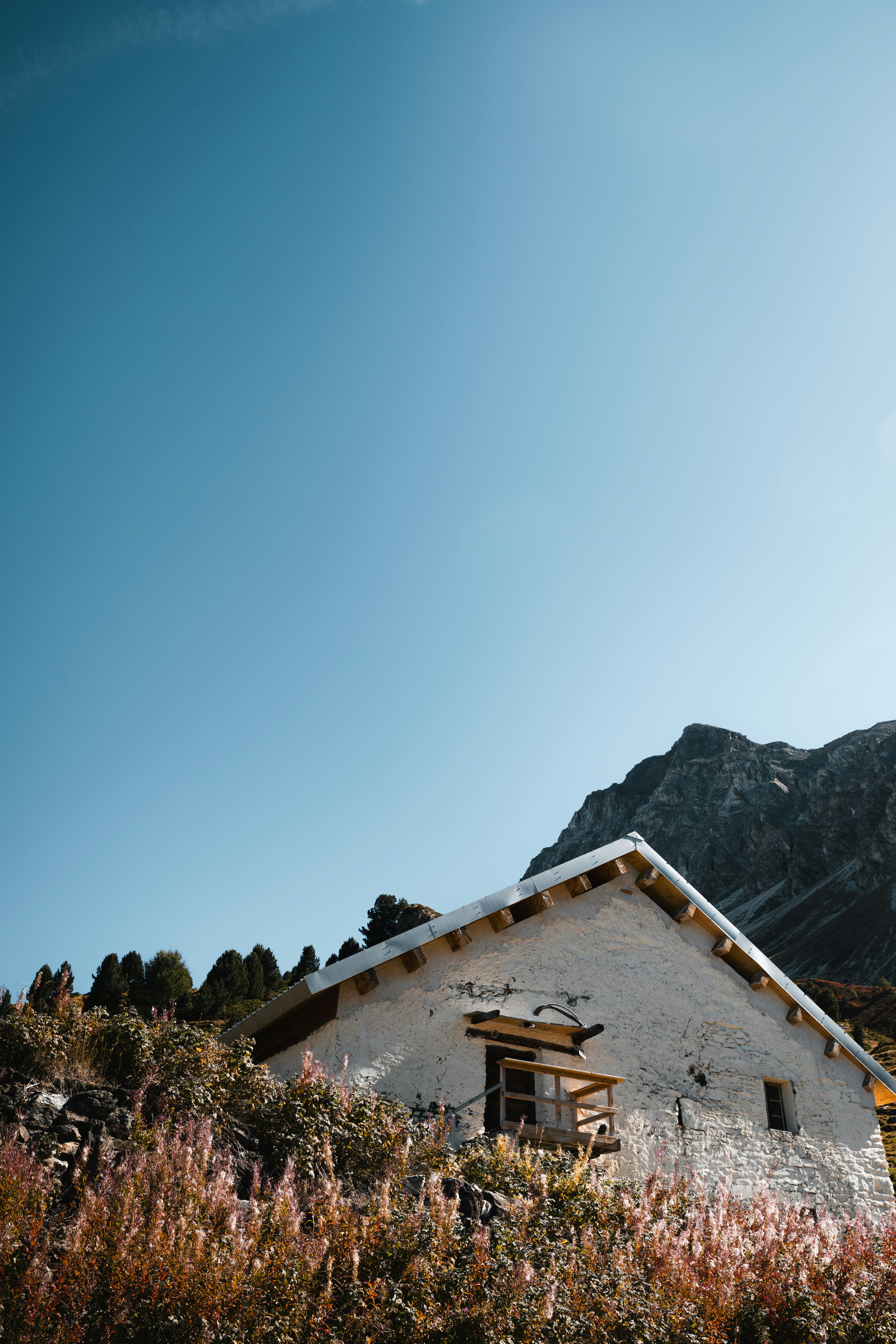 A white stone cabin with a wooden balcony below a rocky mountain peak
