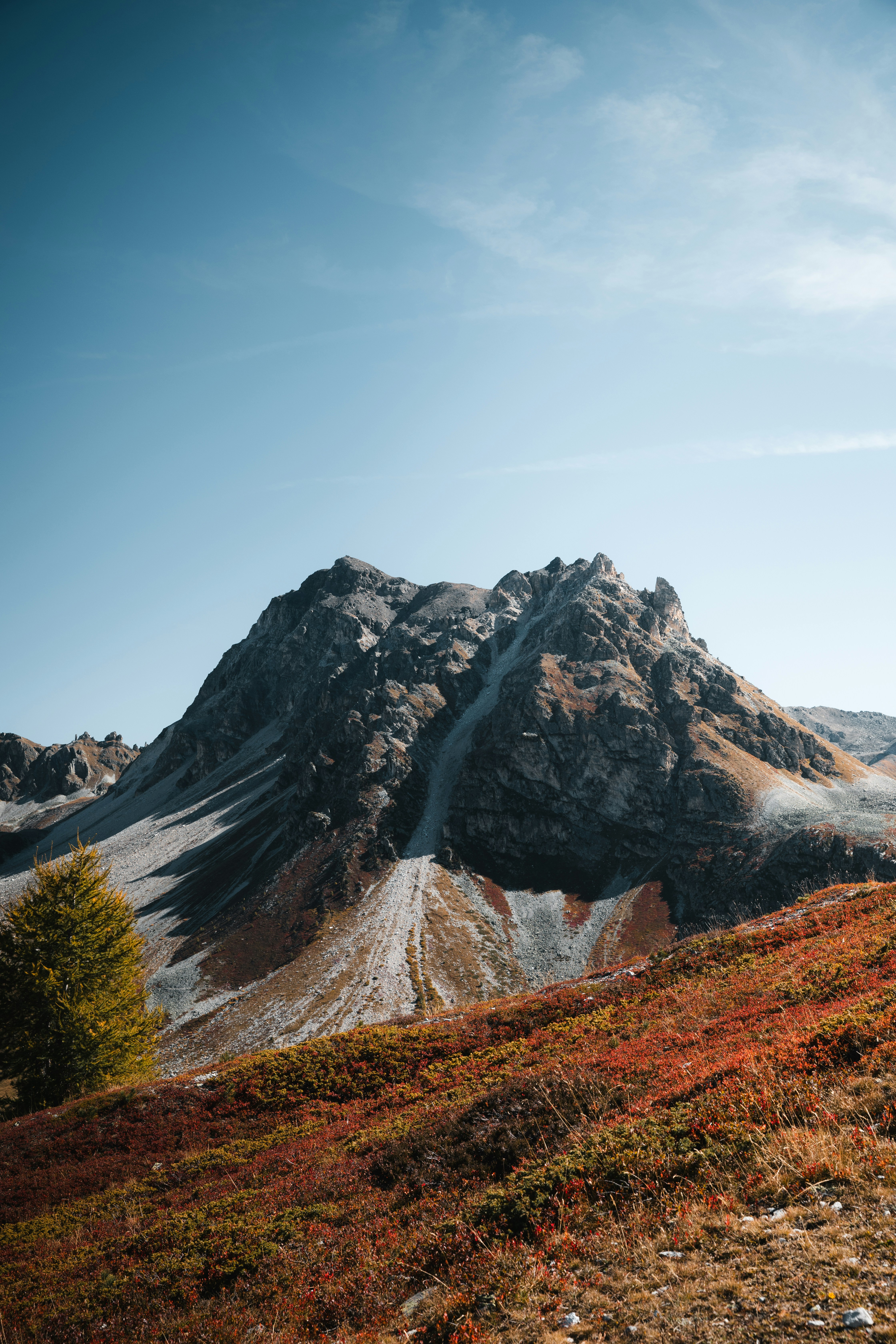 A rocky mountain peak rising above a slope with red and orange autumn foliage