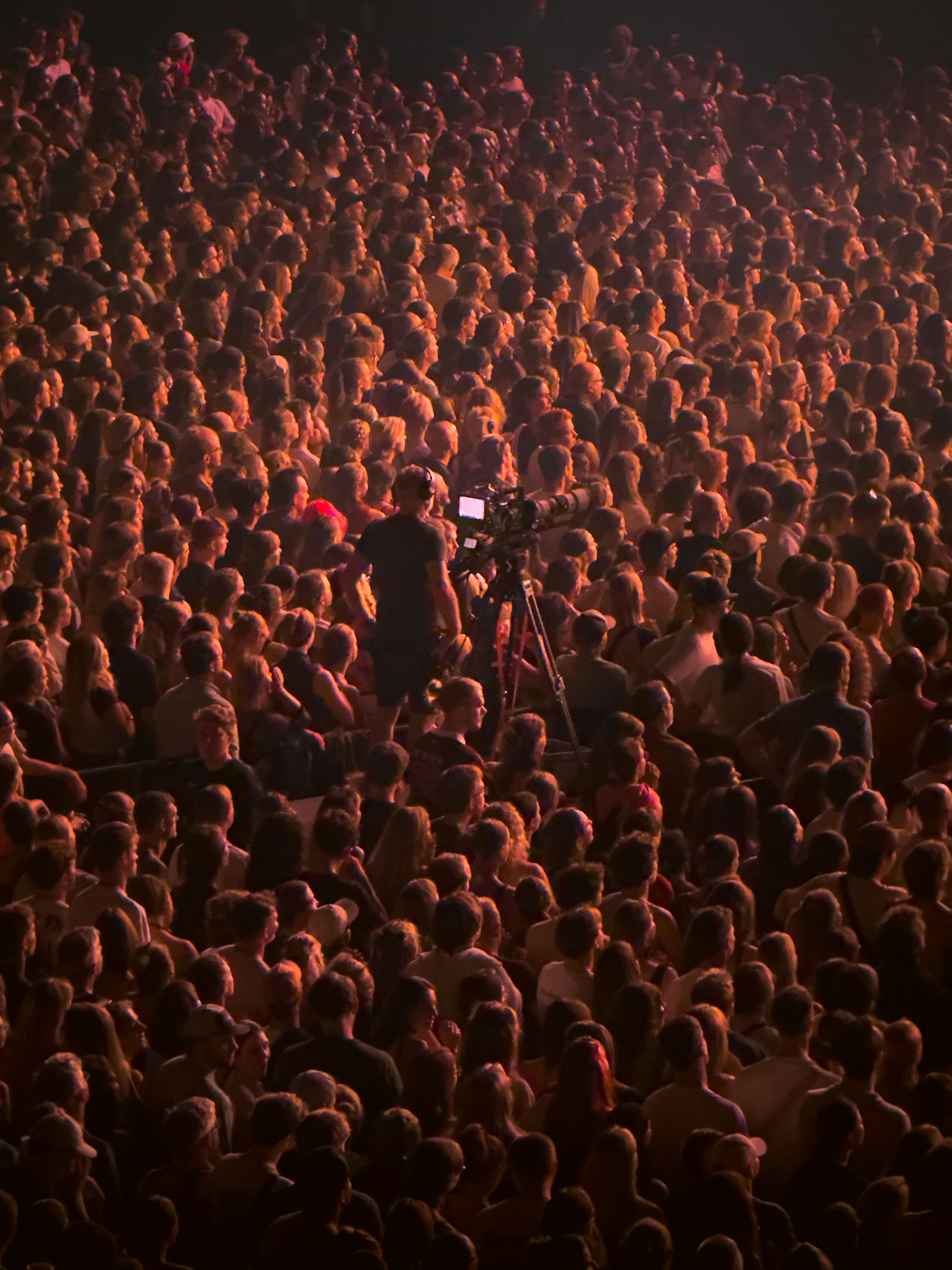 A large crowd of people at a concert with a camera operator filming