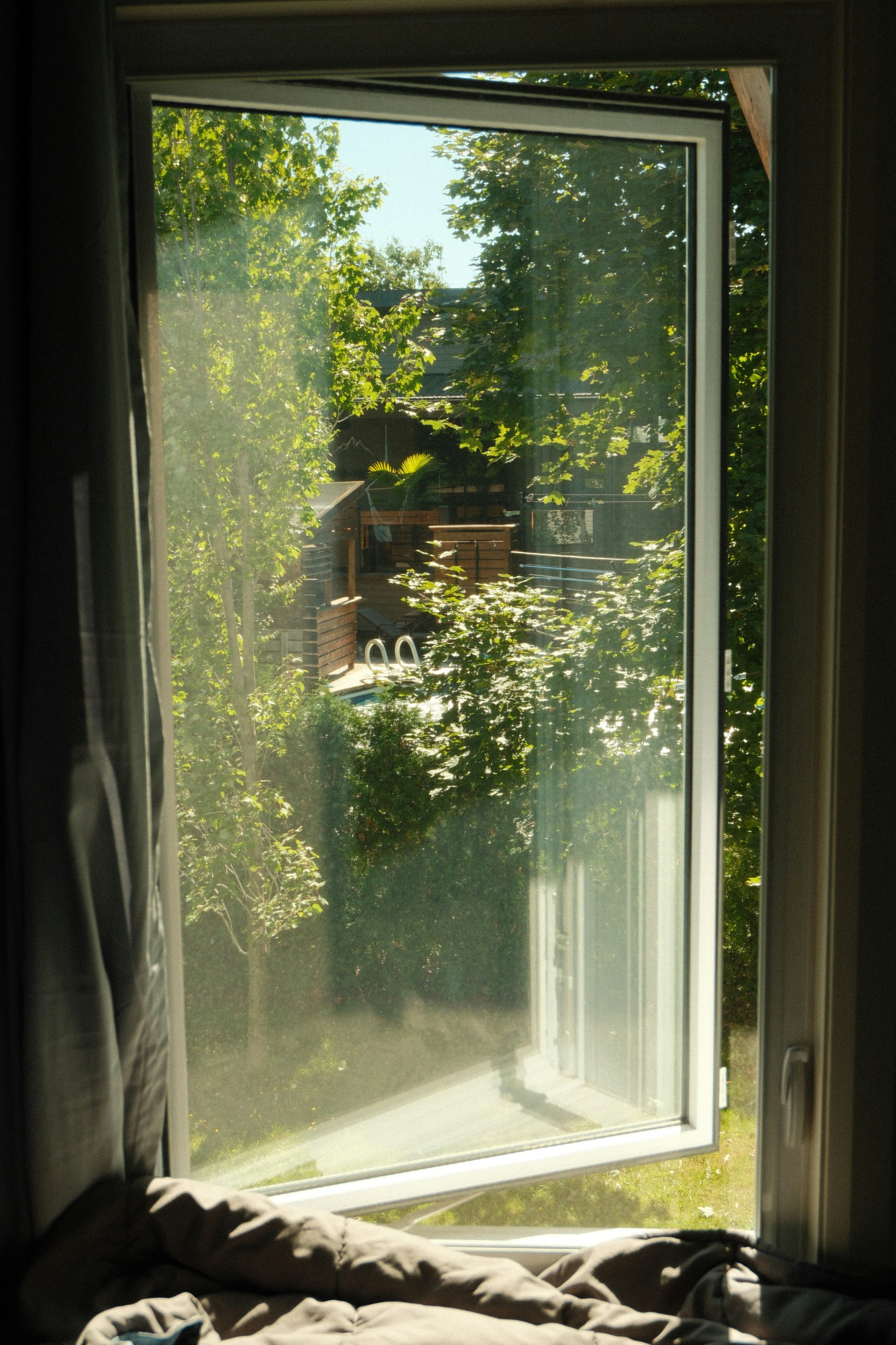 A view through an open window of a sunlit backyard with a swimming pool