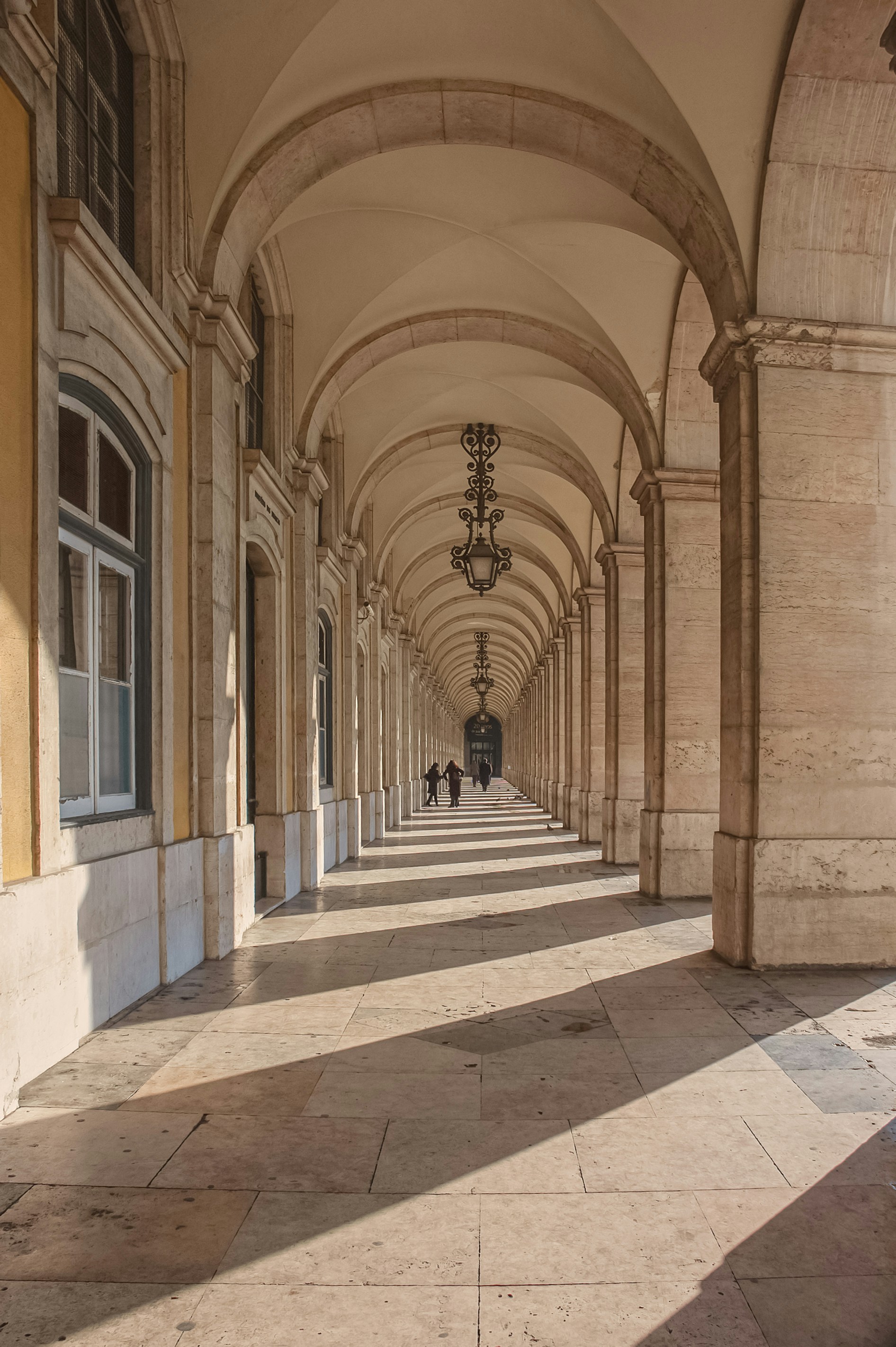 A long stone arcade with arched ceilings and hanging lanterns in Lisbon