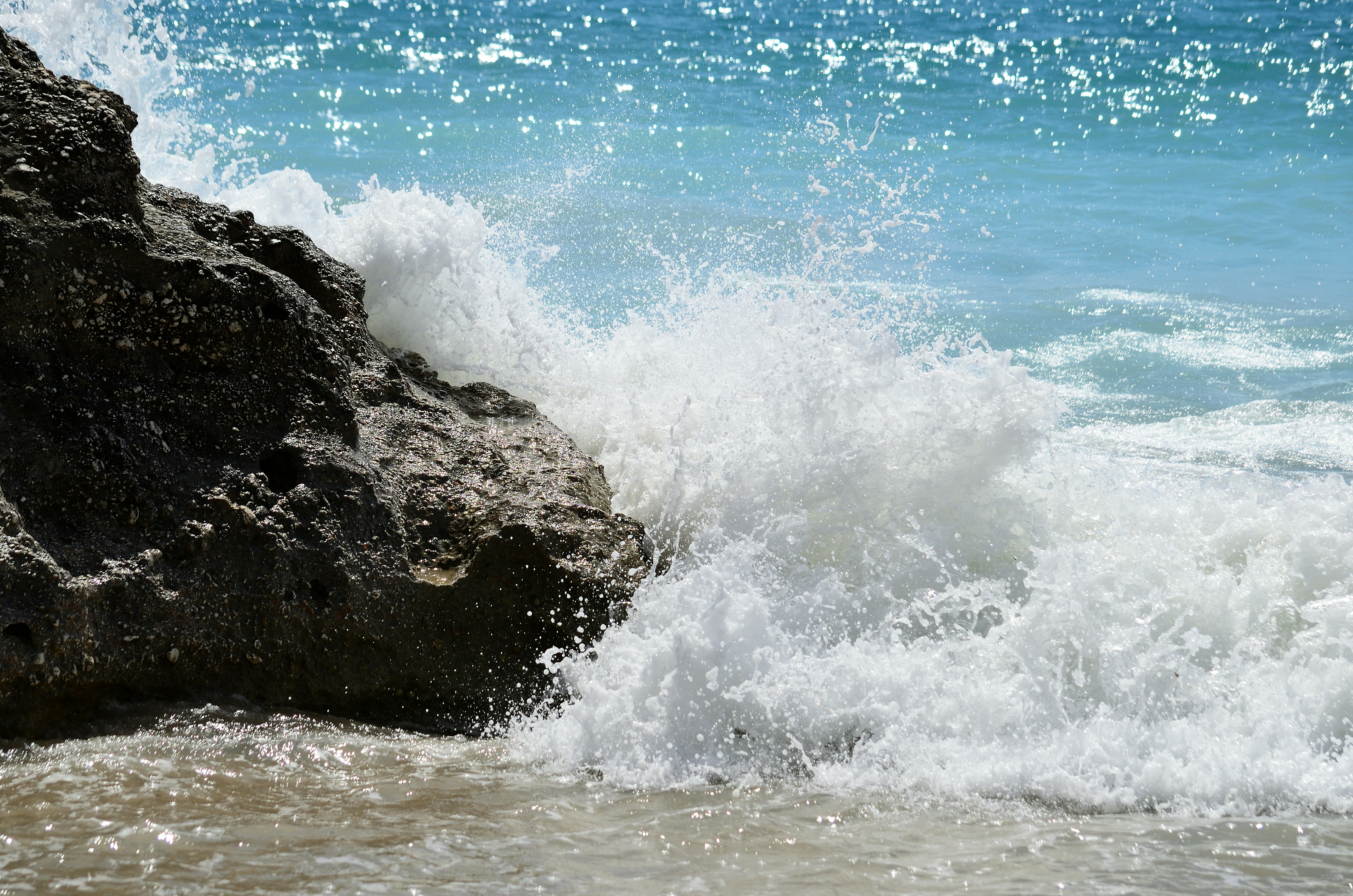 Ocean waves crashing against a dark rocky outcrop on a sunny day