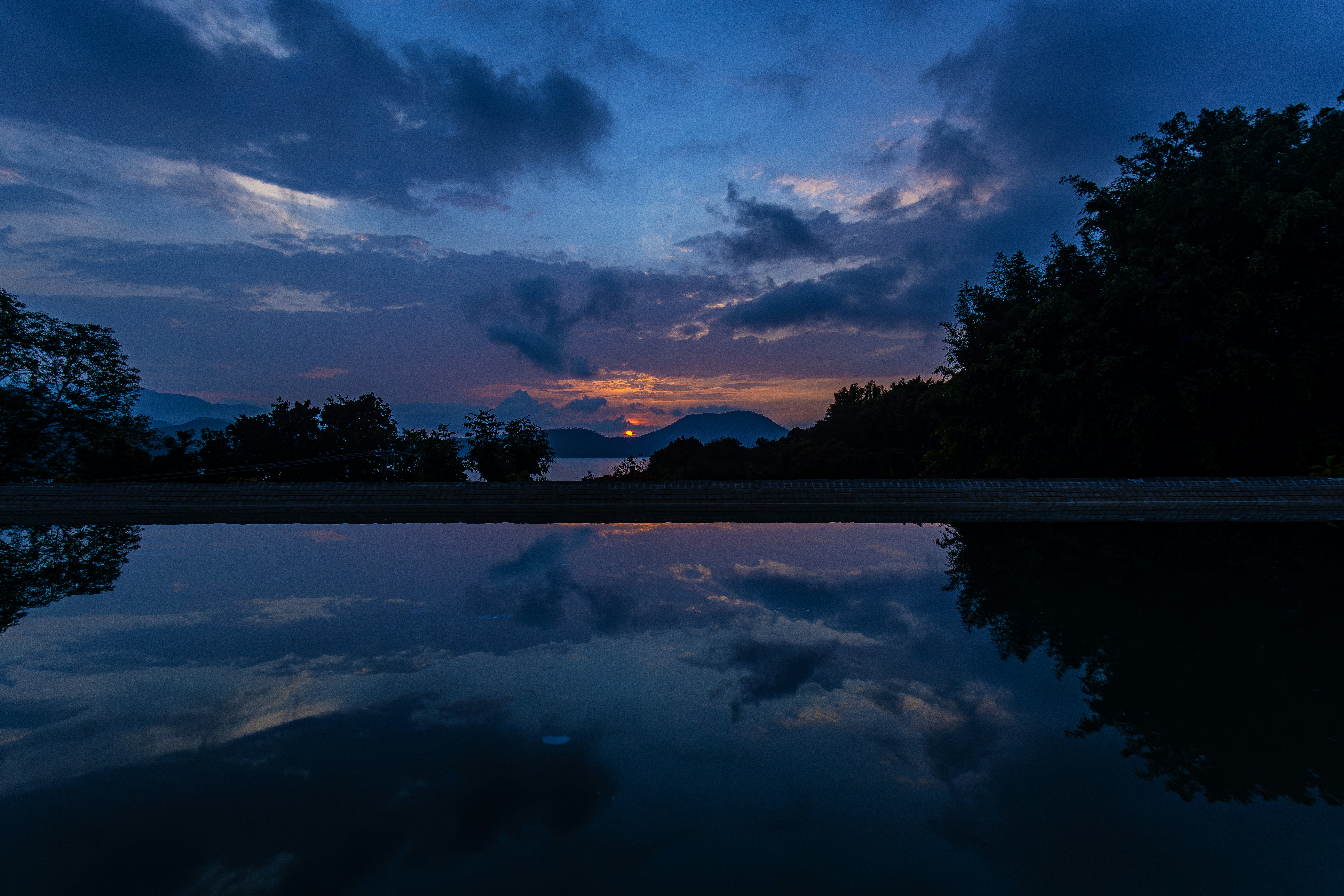 Um céu azul escuro com nuvens refletindo em uma piscina calma de água