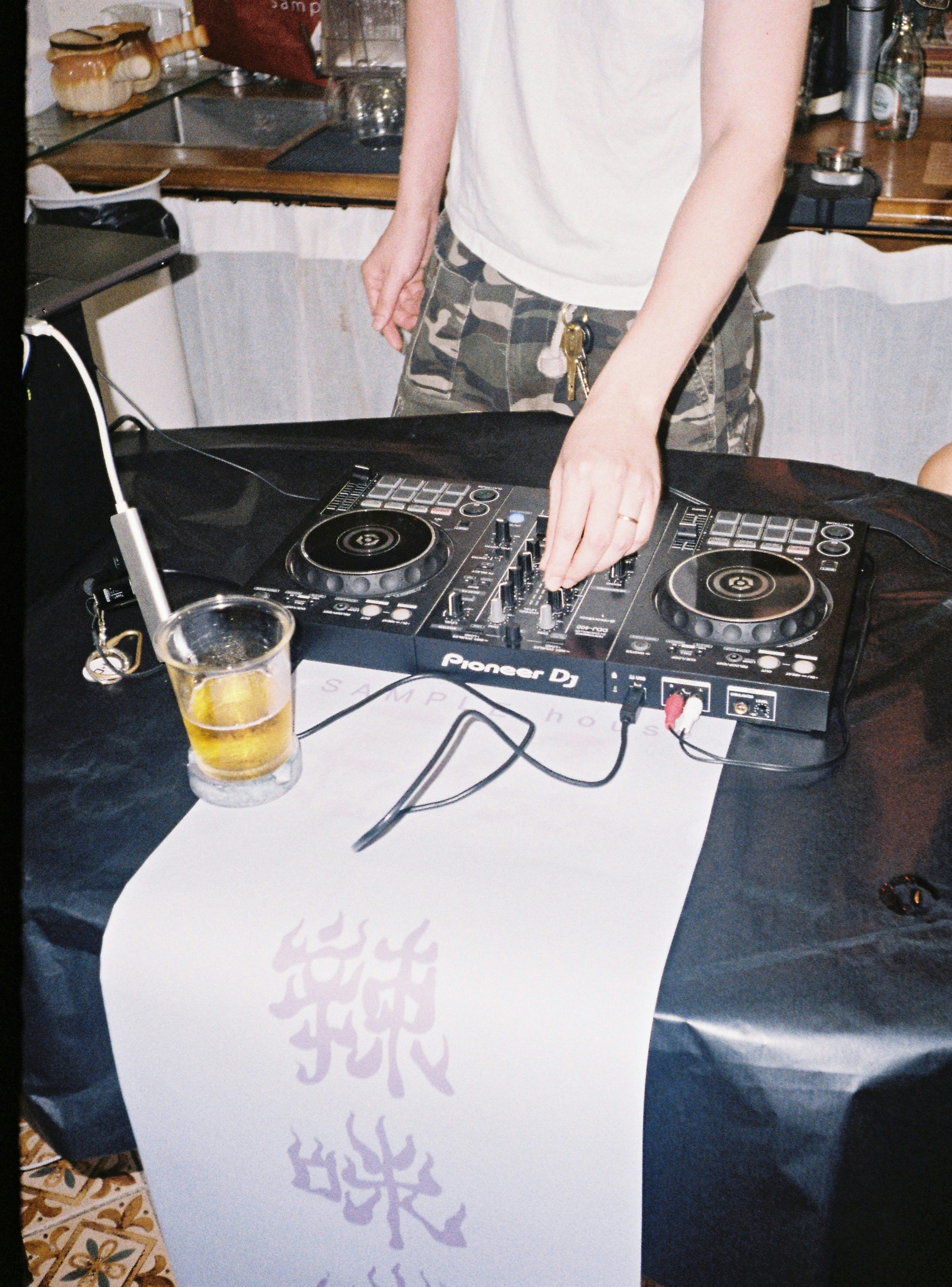 テーブルの上でパイオニアのDJコントローラーを調整し、ビールのグラスを手にしている人