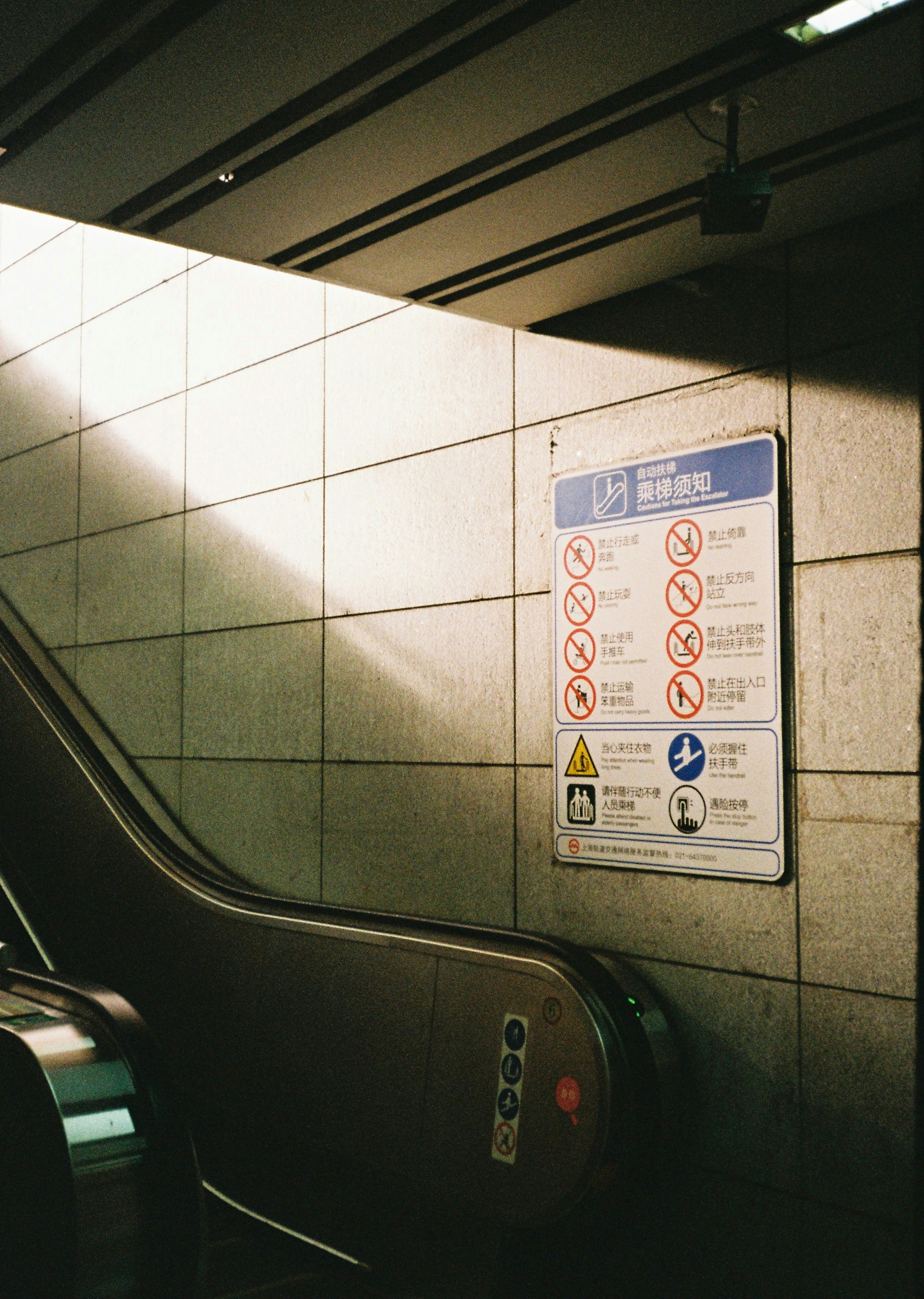 An escalator safety sign on a tiled wall in a subway station