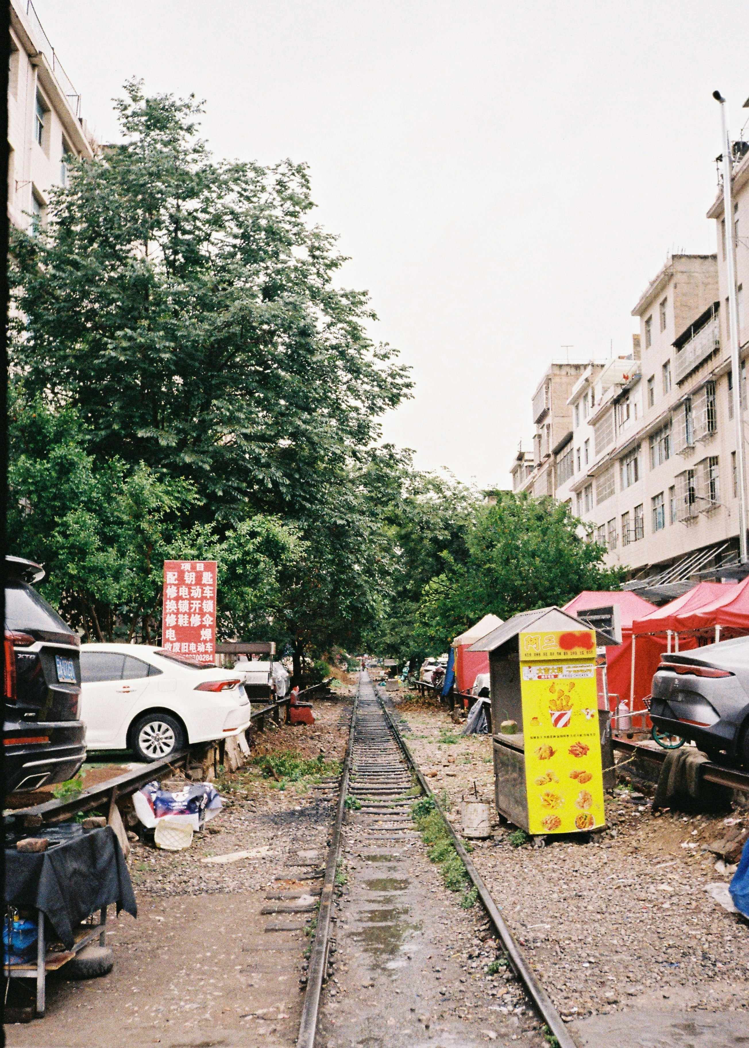 Eisenbahngleise zwischen geparkten Autos und Essensständen in einer Stadt