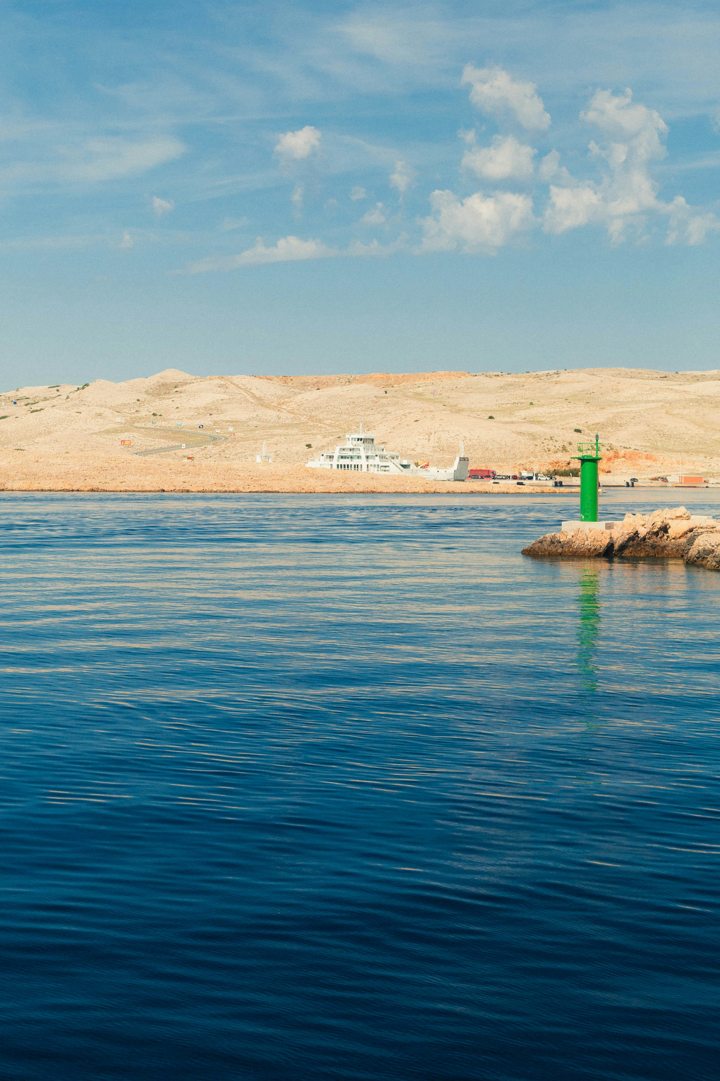 A green navigation beacon on a rocky point with a ferry in the distance