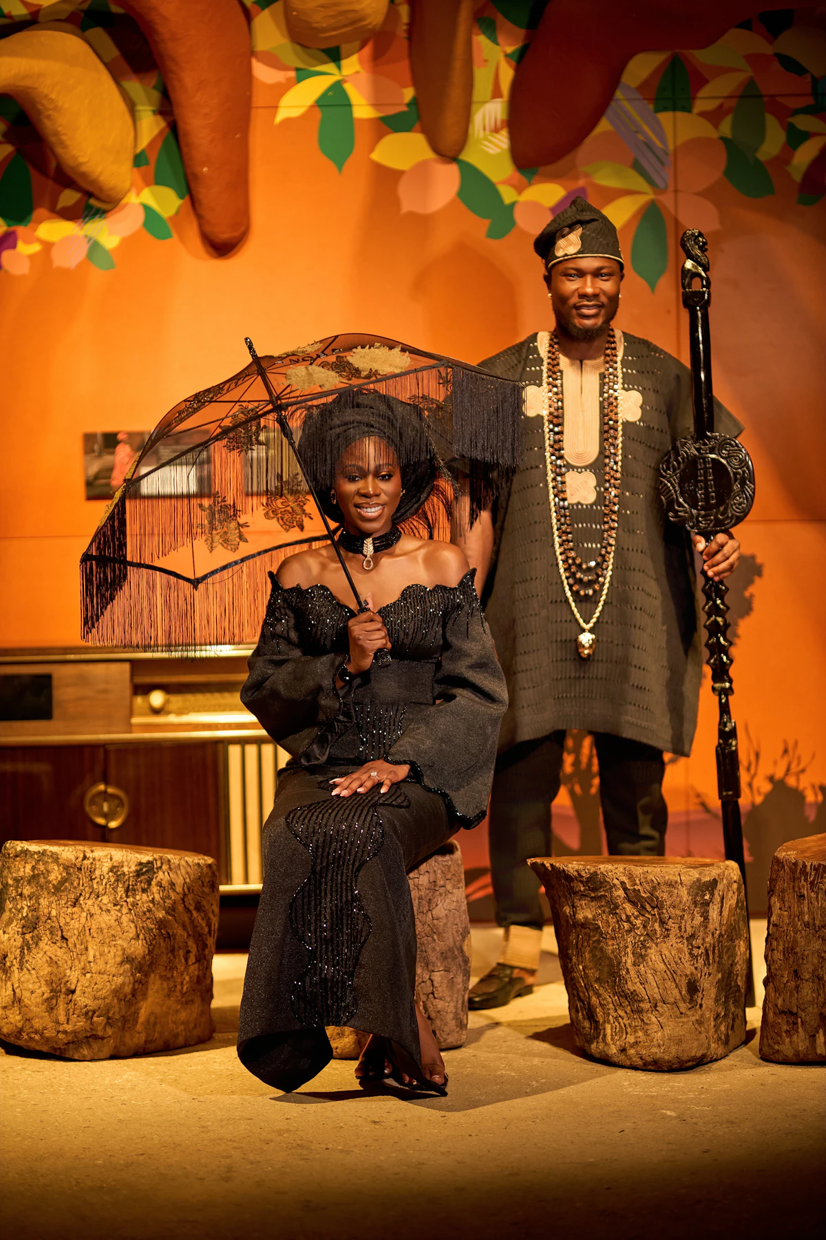 A Nigerian couple in traditional wedding attire, the bride holding a fringed parasol