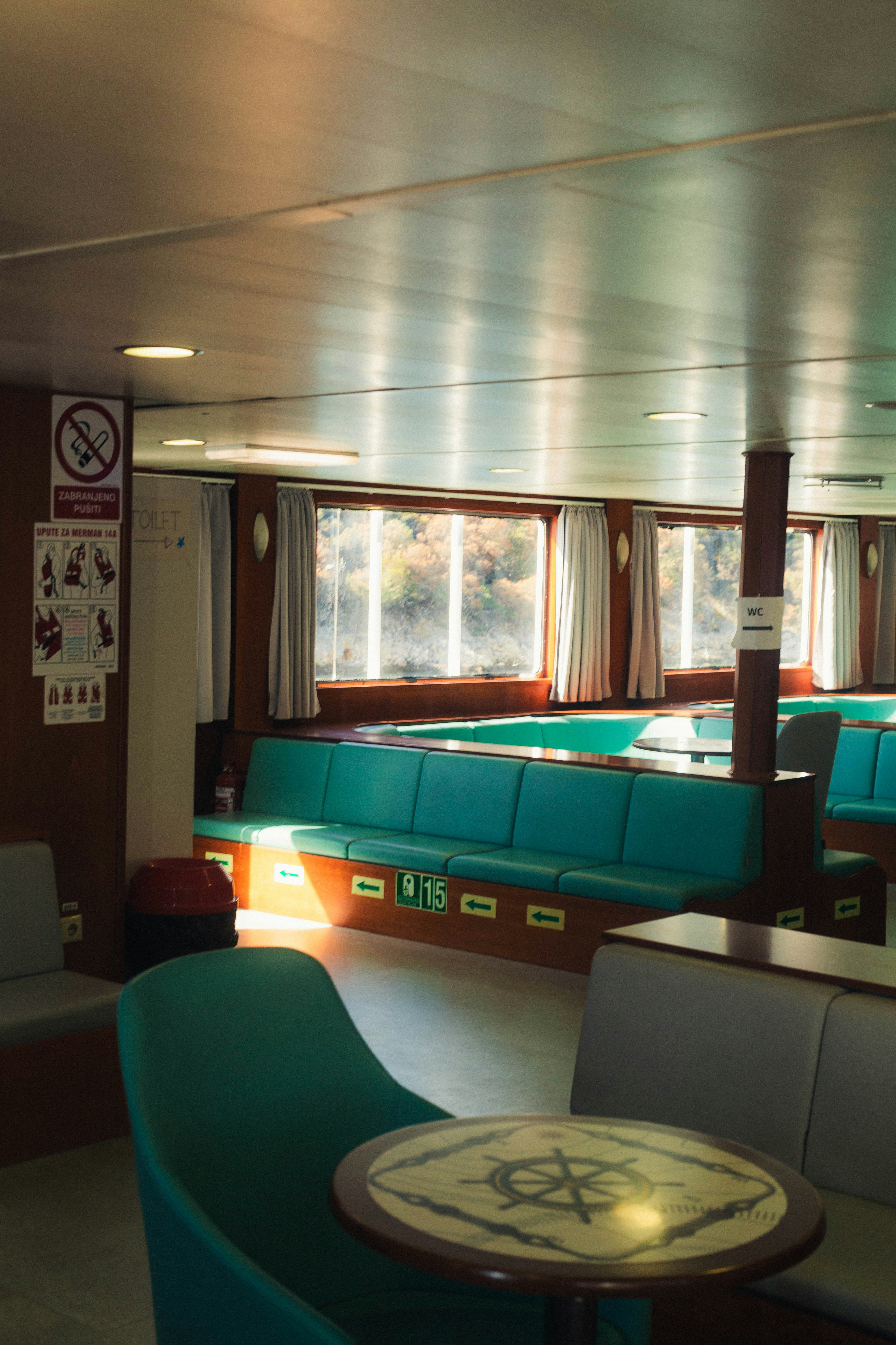 Teal bench seating and a round table inside a ferry cabin with windows